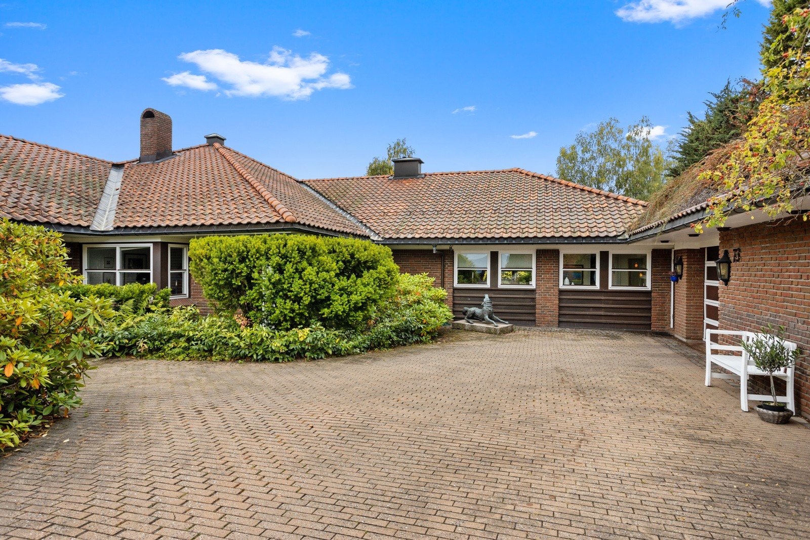 Stor, stenlagt gårdsplass med inngangsparti mot venstre og inngang garasje mot høyre. Galleribilde