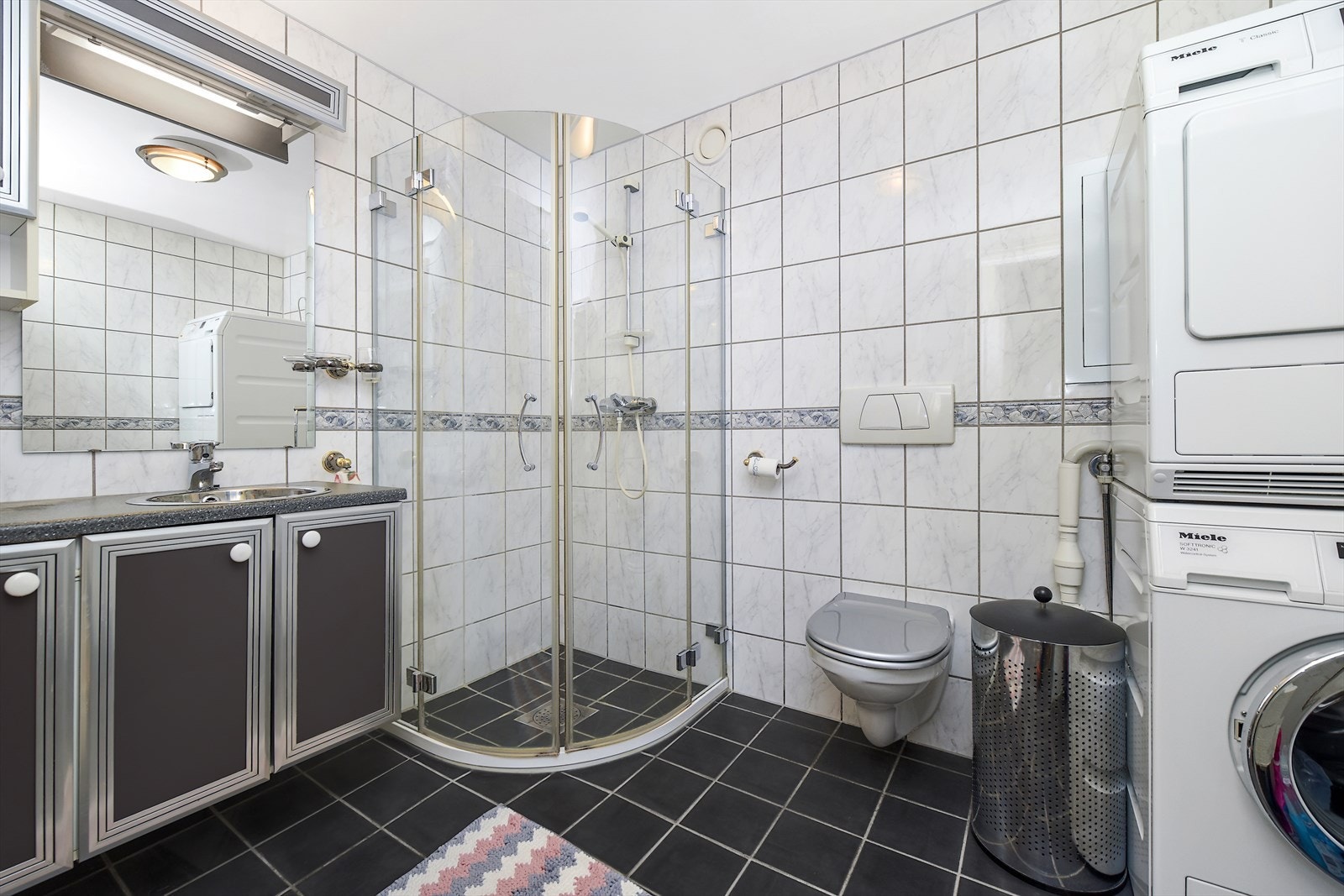 Flislagt bad med dusjhjørne, servantinnredning, vegghengt wc og opplegg for vaskemaskin. Galleribilde