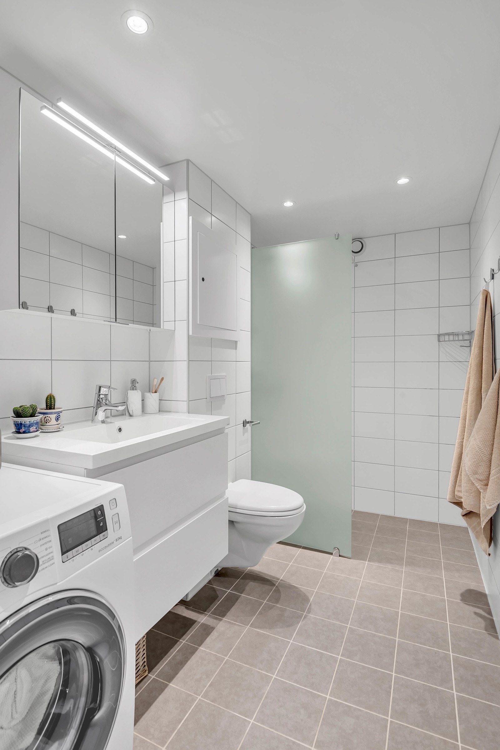 Her har du dusjhjørne med glassvegg, vegghengt toalett og opplegg for vaskemaskin. Galleribilde