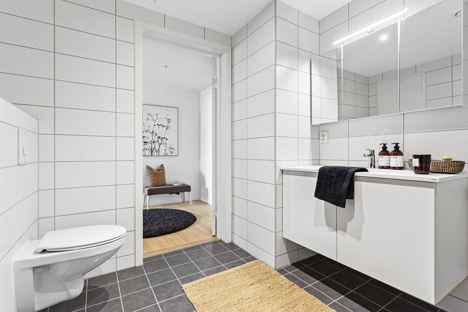 Badet er innredet med vegghengt toalett, servant med skap og dusjnisje med innfellbare glassdører. Galleribilde