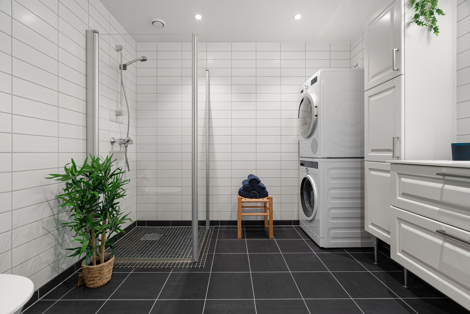 Badet fremstår romslig med stort dusjhjørne, vegghengt toalett og god plass til vaskemaskin og tørketrommel.