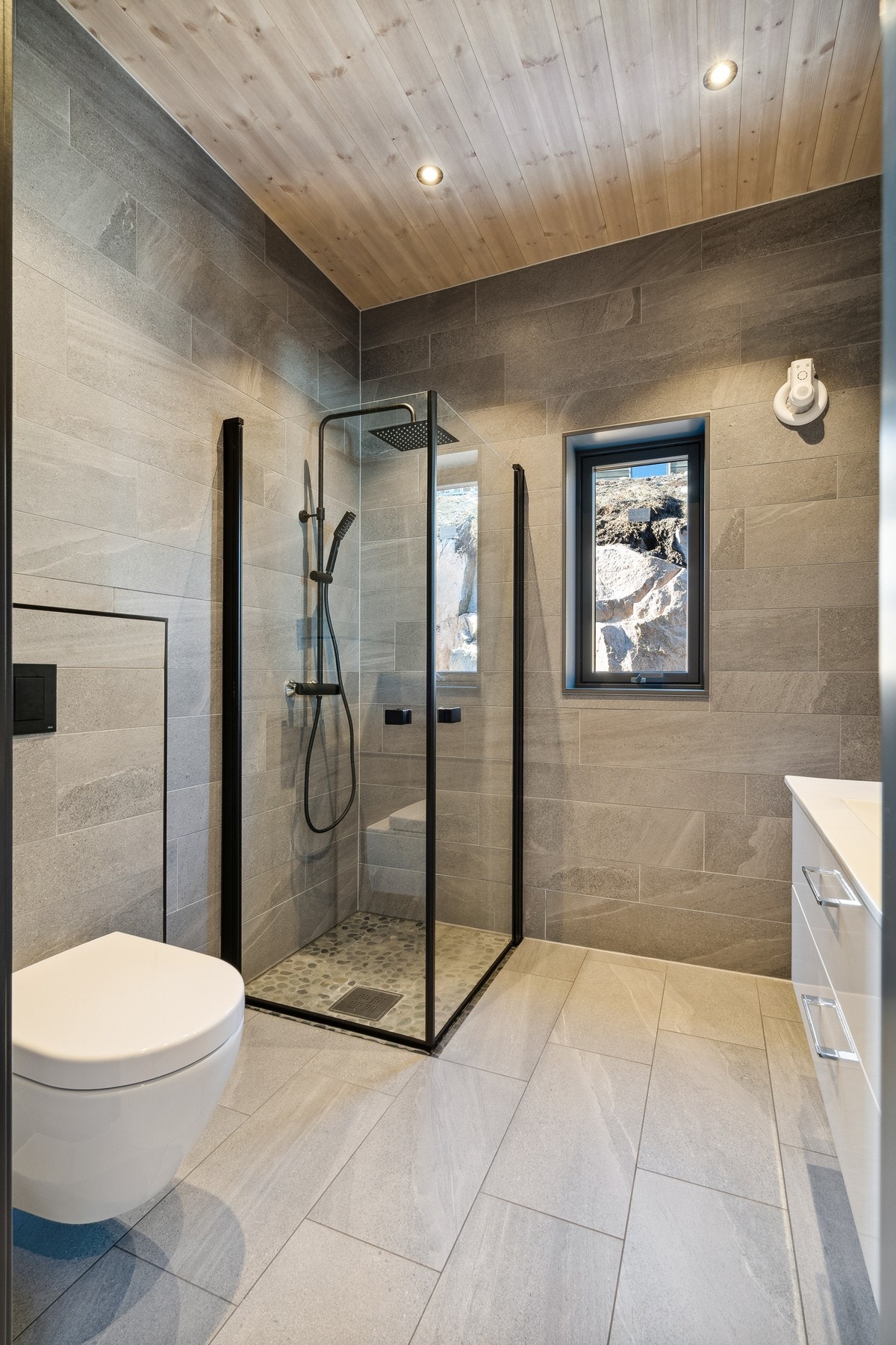 Vegghengt toalett og et stilfullt dusjhjørne med glassdør og svarte detaljer. Galleribilde