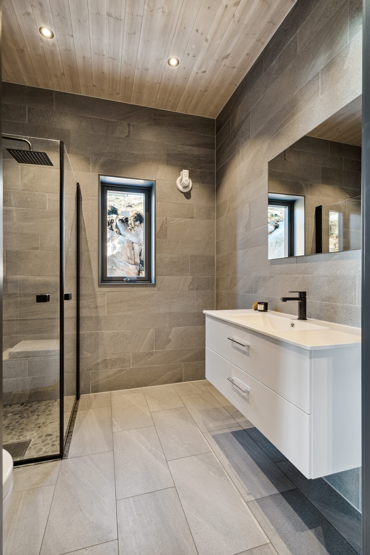 Her er det mørke fliser på vegger og gulv. I taket er det spotter og likt panel som i resten av hytten. Galleribilde