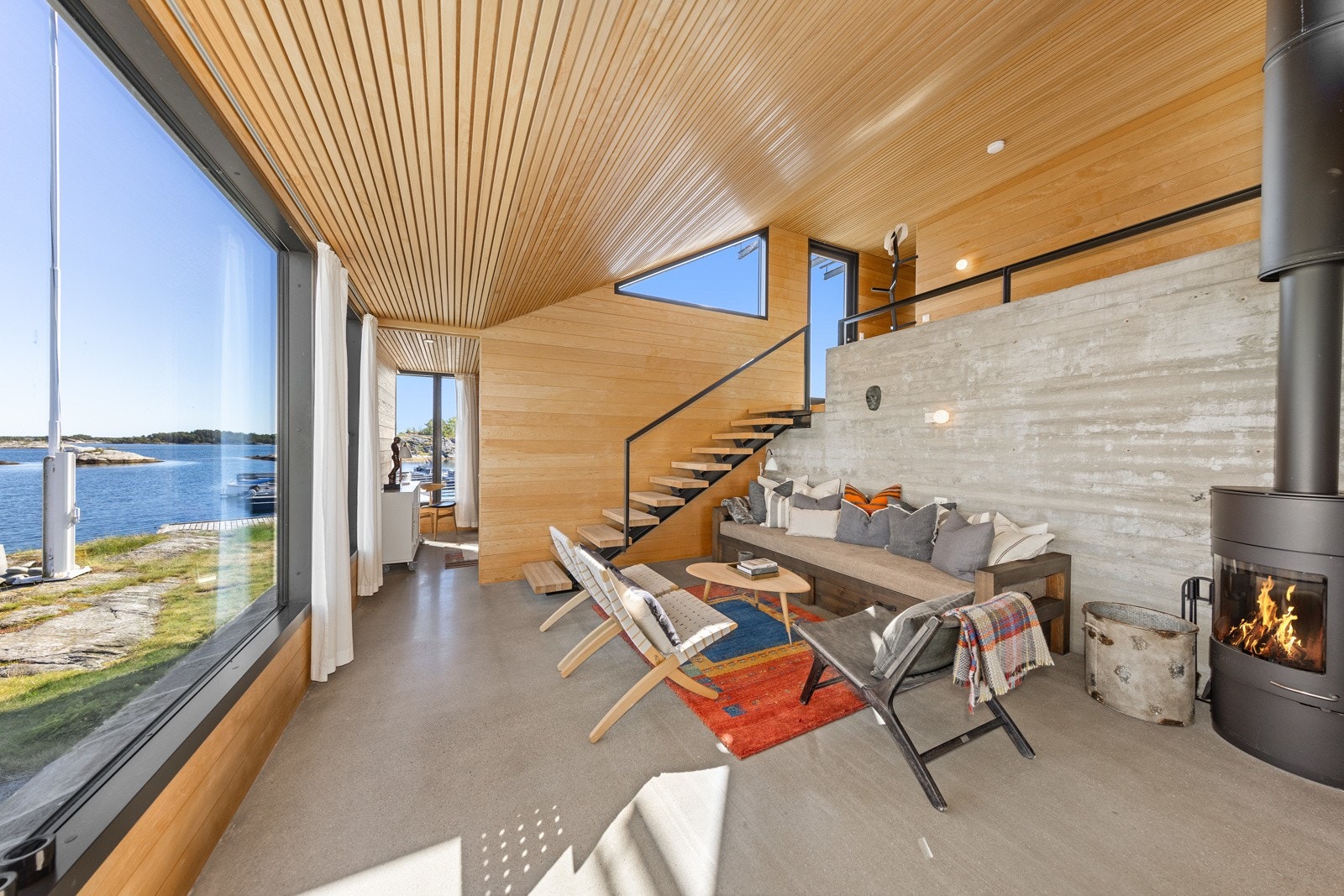 Stue med moderne peisovn og store glassfasader mot sjøen Galleribilde
