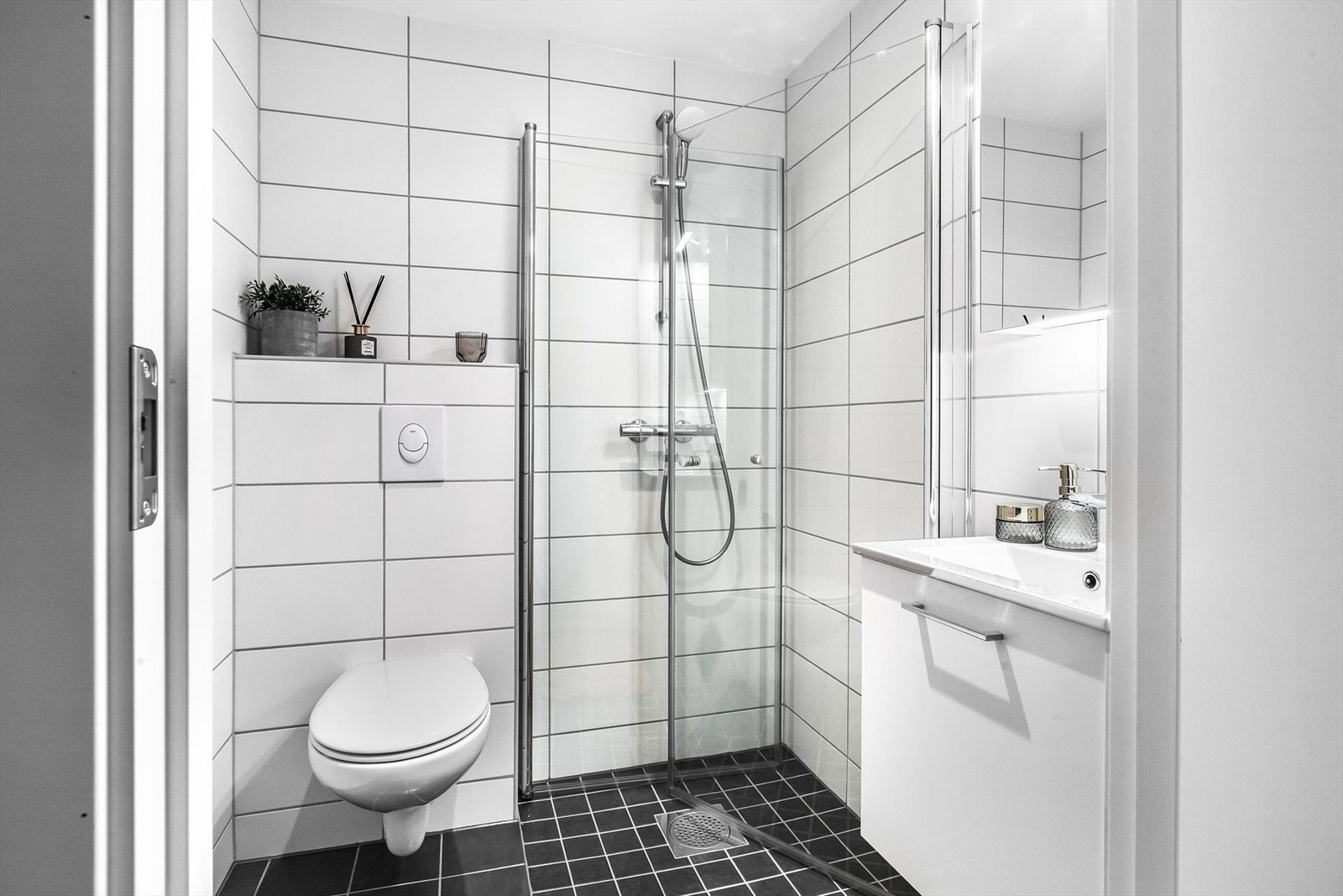 Pent flislagt baderom i tidløse farger. Badet er innredet med vegghengt toalett, servant med skap og dusjnisje med innfellbare glassdører. Speilskap med belysning i overkant av servant, samt varme i gulv. Galleribilde