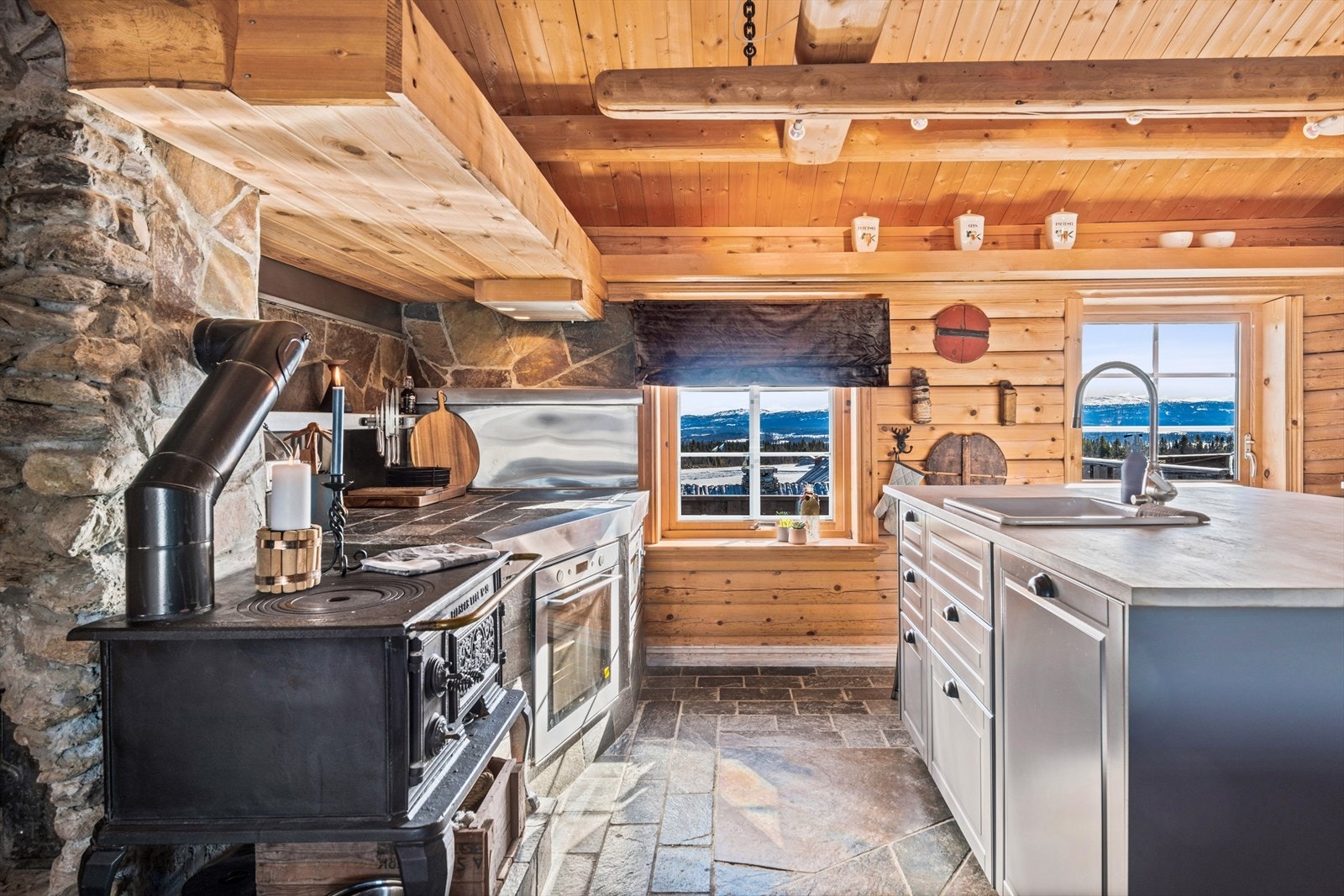 Sjarmerende kjøkken med tømmervegger, eldre vedovn og mer moderne innredning med integrerte hvitevarer Galleribilde