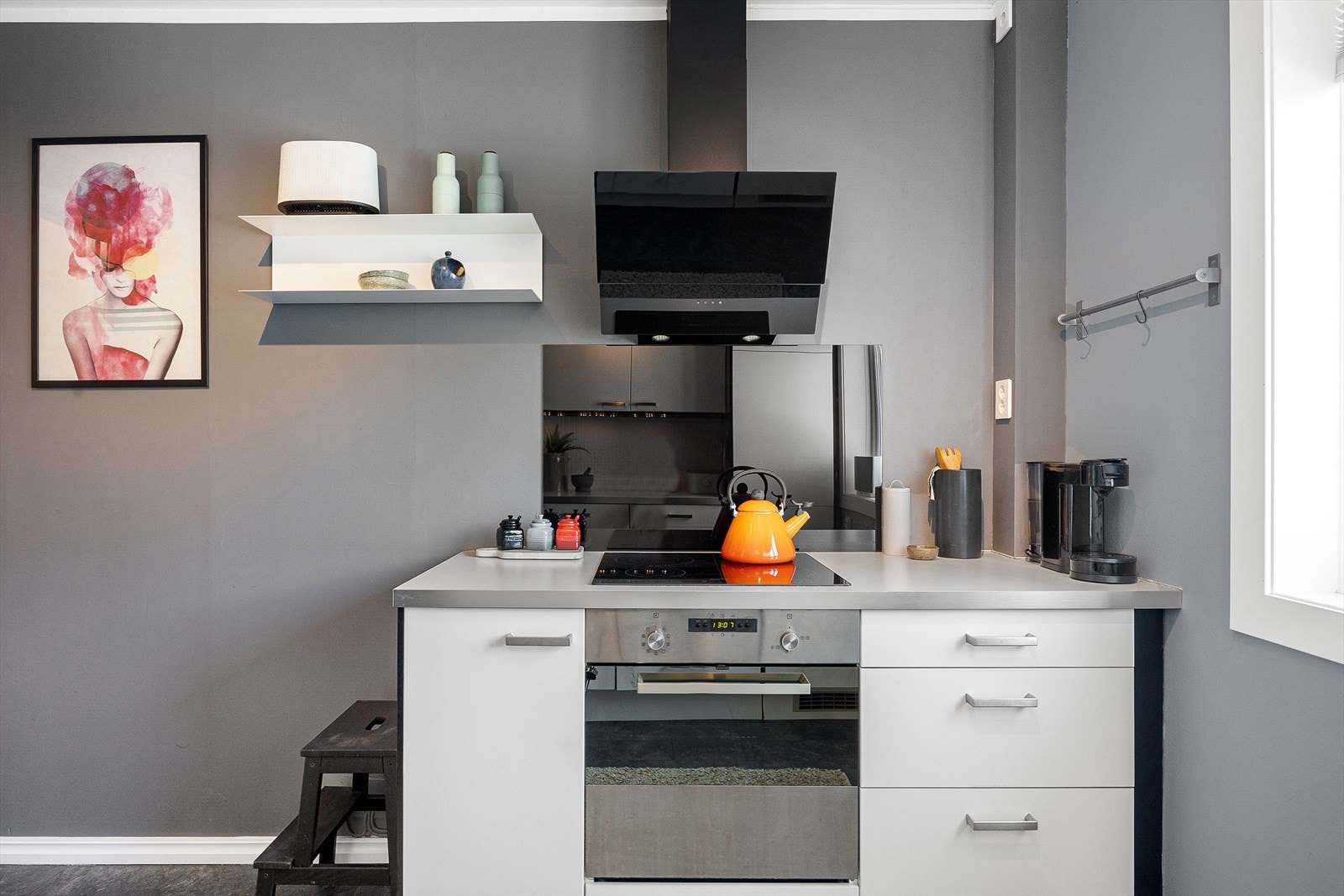 Innredning med glatte, hvite fronter, benkeplate i laminat, fliser over benkeplate på vaskesiden og plate på vegg bak stekesone Galleribilde