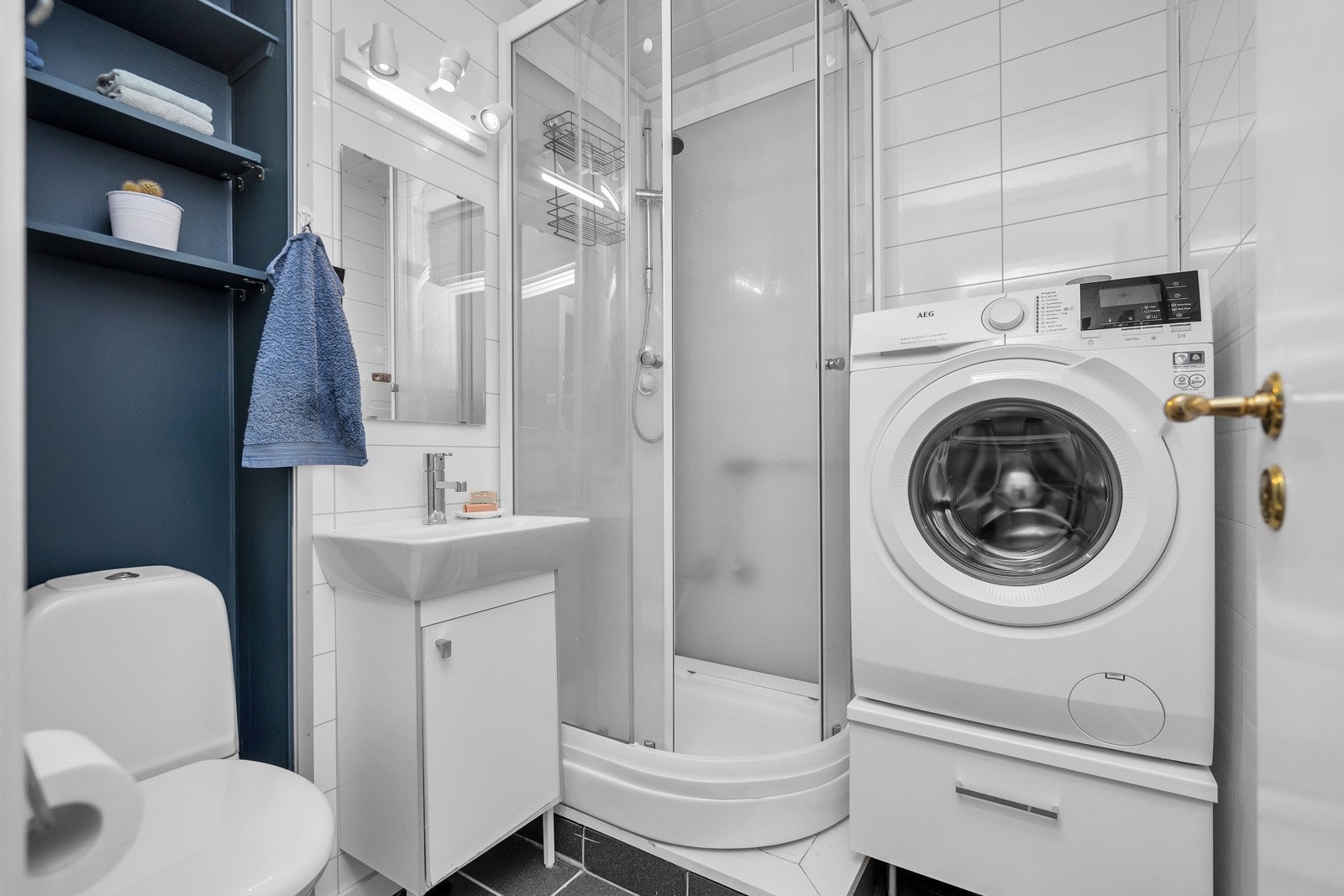 Flislagt bad med toalett, servant med innredning, dusjkabinett og opplegg til vaskemaskin Galleribilde