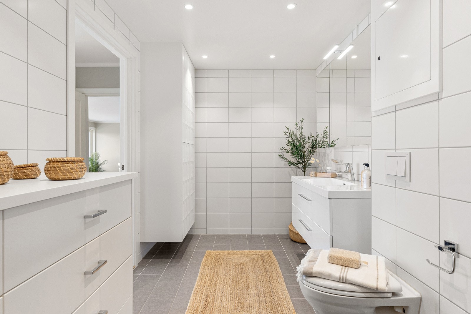 Badet er innredet med vegghengt klosett, servant med underskap, overskap med speil og dusjhjørne med dører i glass. Galleribilde