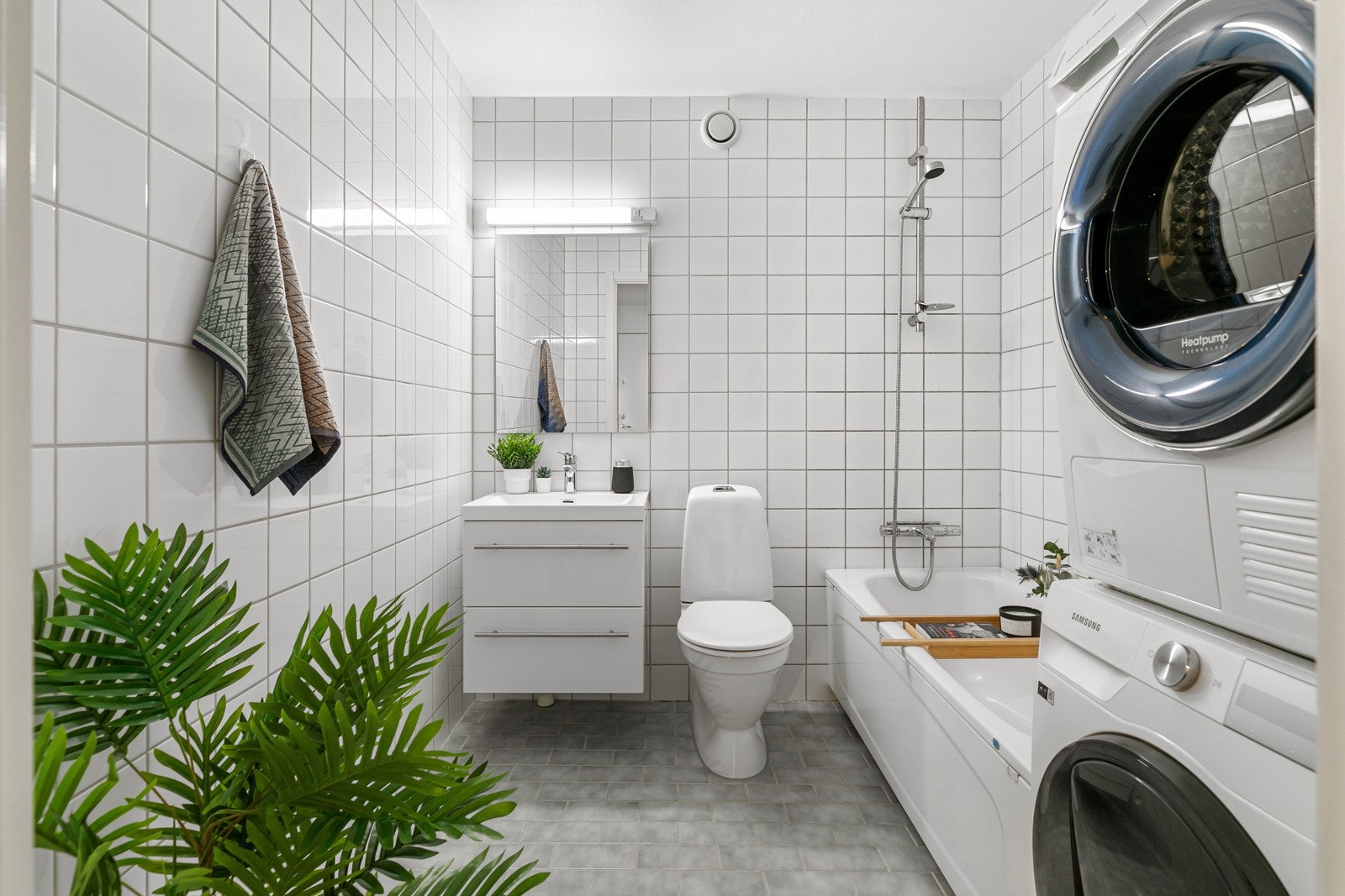 Pent flislagt bad innredet med varmekabler, frittstående badekar, veggmontert servantinnredning og gulvstående klosett. opplegg for vaskemaskin Galleribilde