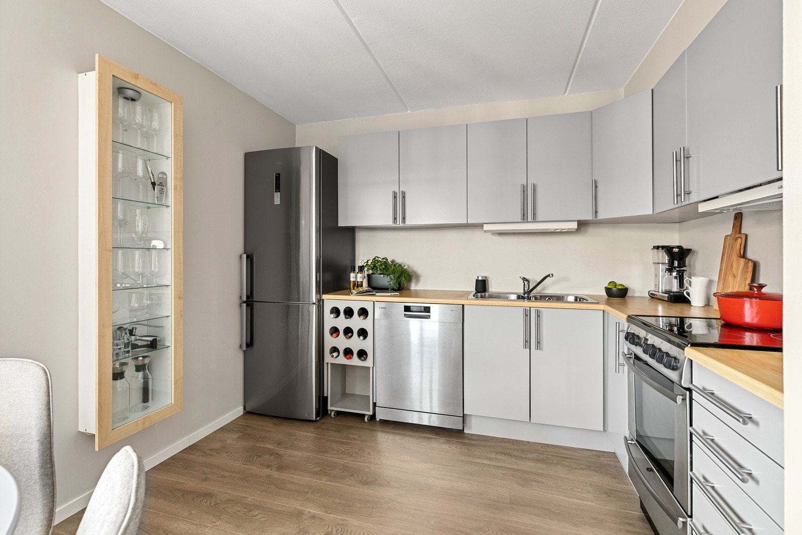 Kjøkkeninnredning med malte slette fronter, overskap og benkebelysning. Krafitg benkeplate med nedfelt stålkum og ett-greps armatur i krom Galleribilde