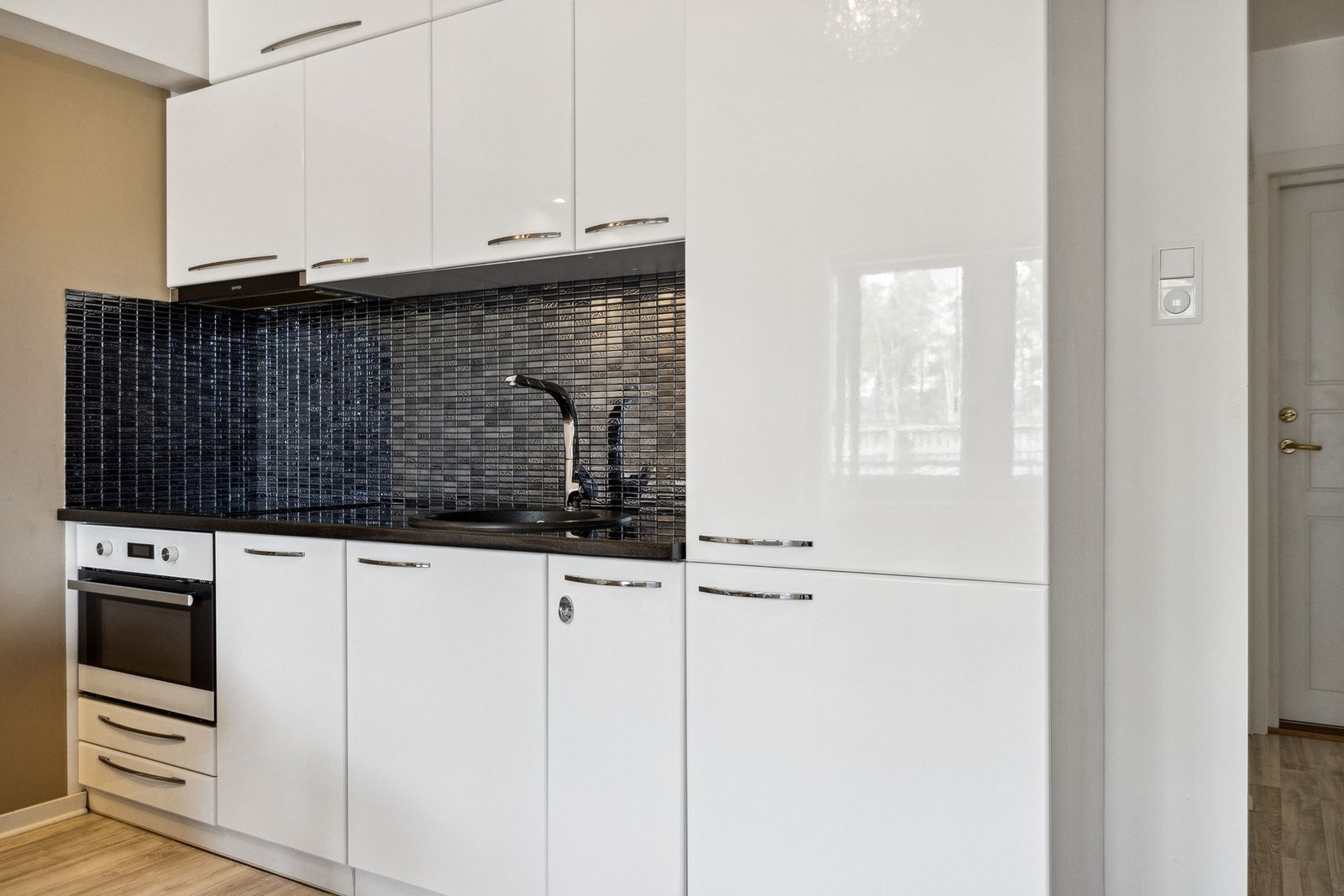 Kjøkken med hvite fronter i høyglans og benkeplate i granitt. Kjøkkenet har innebygget komfyr med induksjonstopp og mikrobølgefunksjoner i stekeovnen, oppvaskmaskin og kjøle/fryseskap. Galleribilde