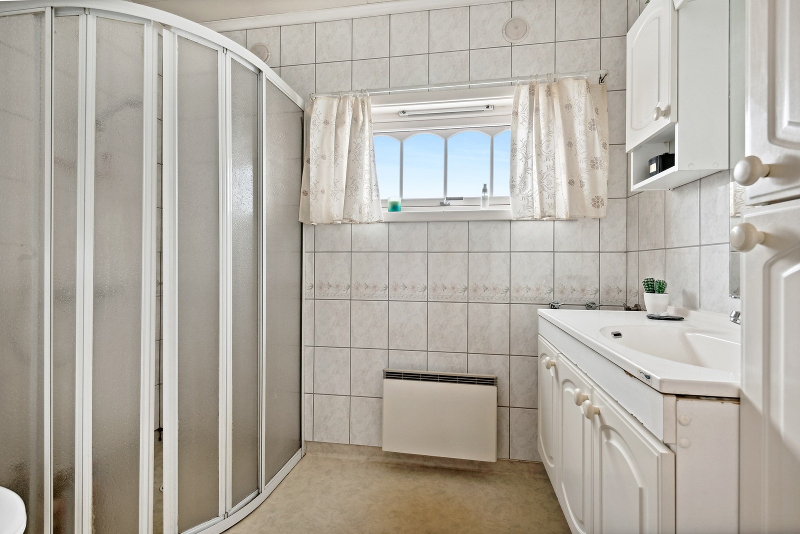 Badet består av belegg på gulv, fliser på vegger. Servant på underskap, wc, dusjhjørne. Badet trenger en oppgradering for å imøtekomme krav til dagens bruk. Galleribilde