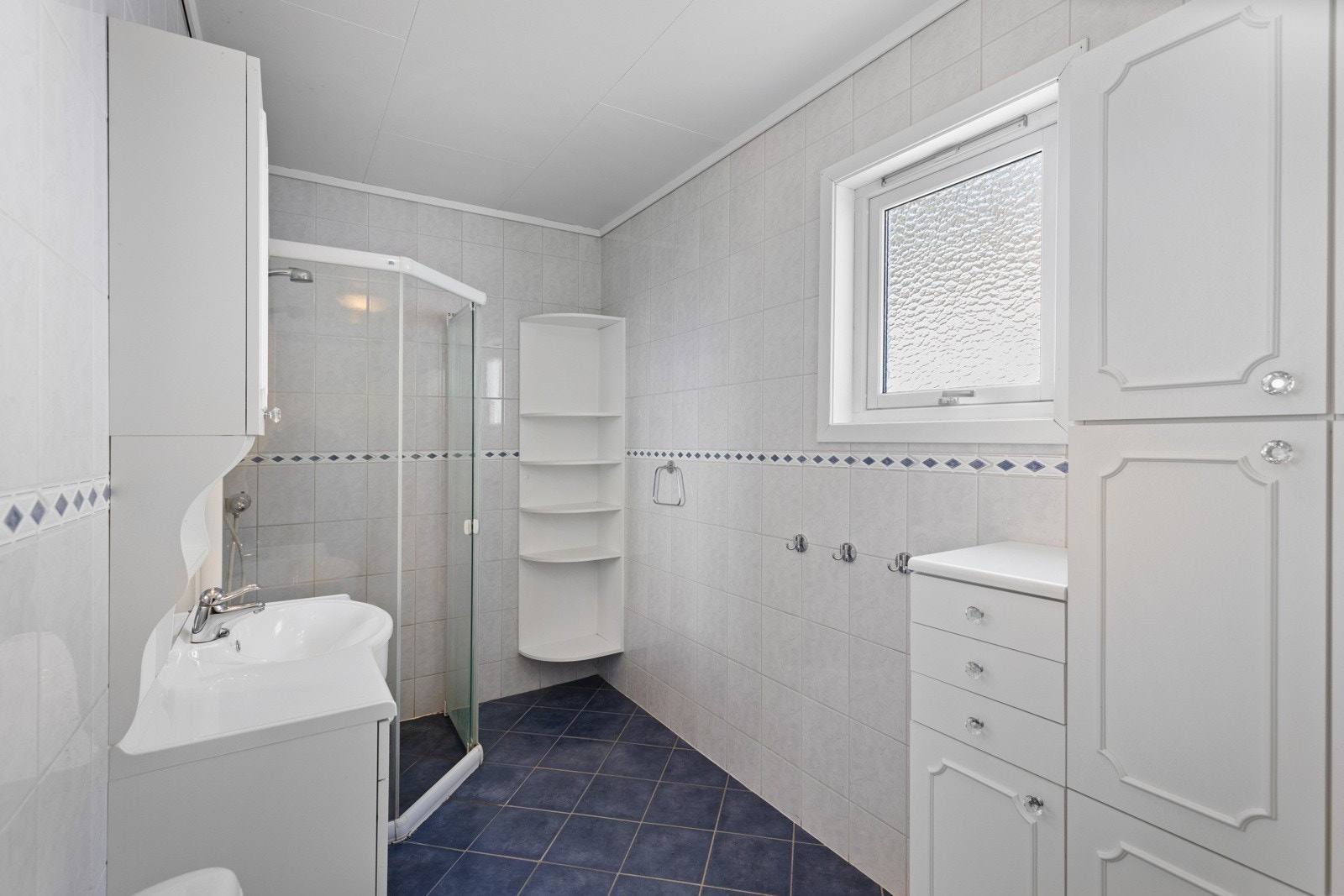 Badet har flislagt gulv med nedstøpte varmekabler og fliskledde vegger. Det er montert dusjnisje med glassvegger, wc, baderomsinnredning med nedfelt servant og skapinnredning med profilerte fronter Galleribilde