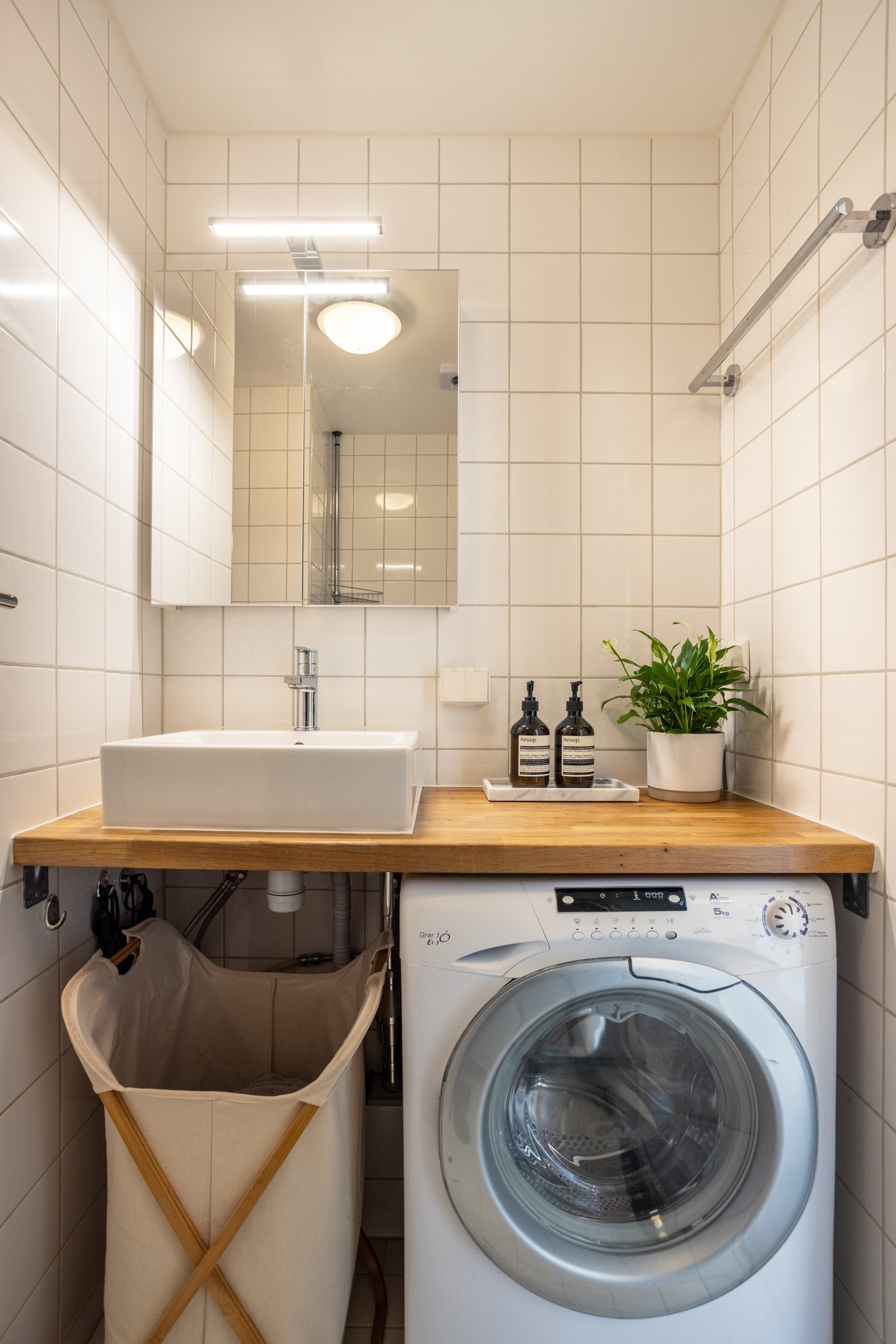 Veggmontert speilskap og heltre benkeplate med utenpåliggende vask og ett-greps armatur i krom. Opplegg for vaskemaskin Galleribilde