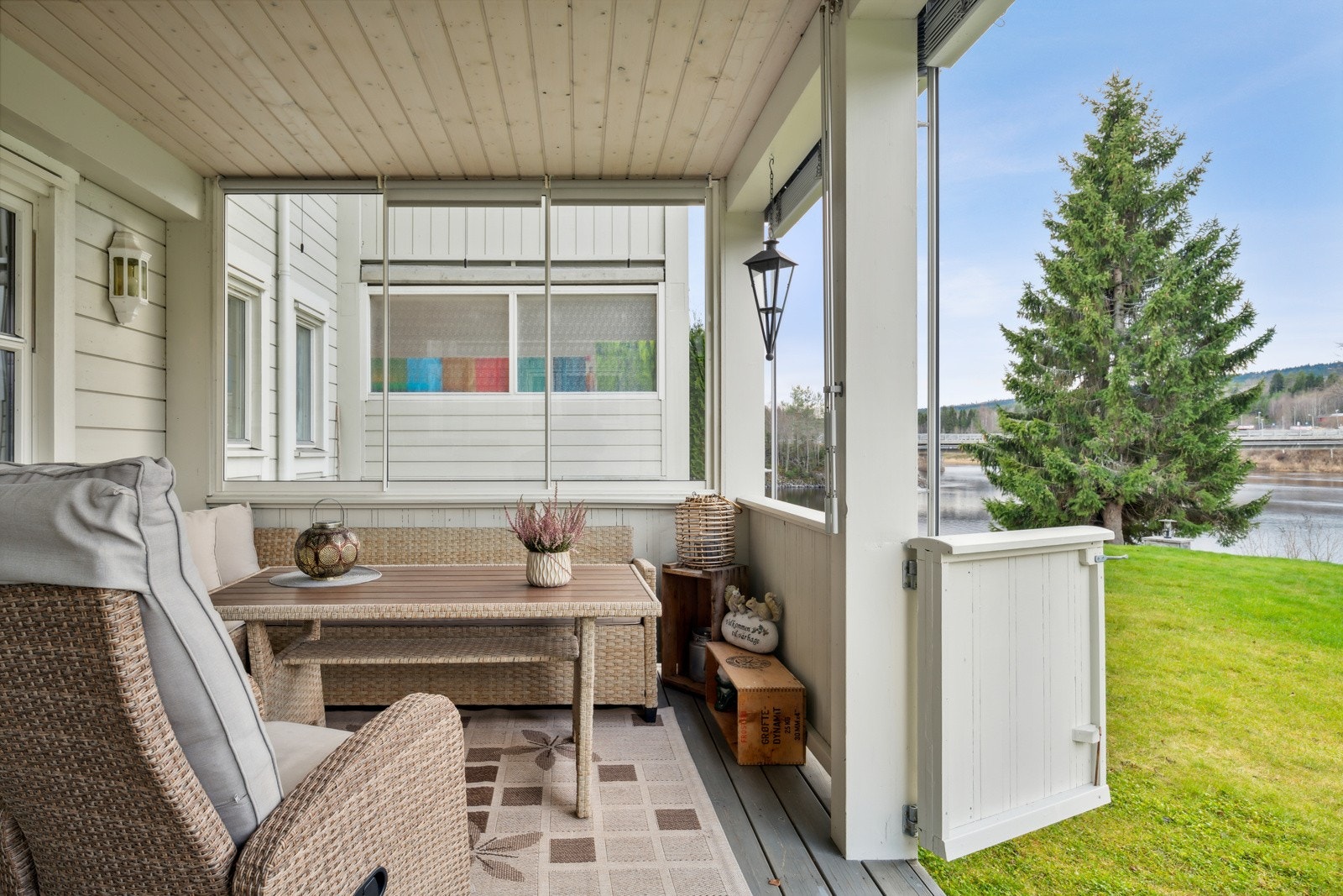 Terrassen er overbygget, har terrassebord på gulv og glassfelt på sidene. Det er montert solskjerming i form av rullegardiner og persienner. Galleribilde