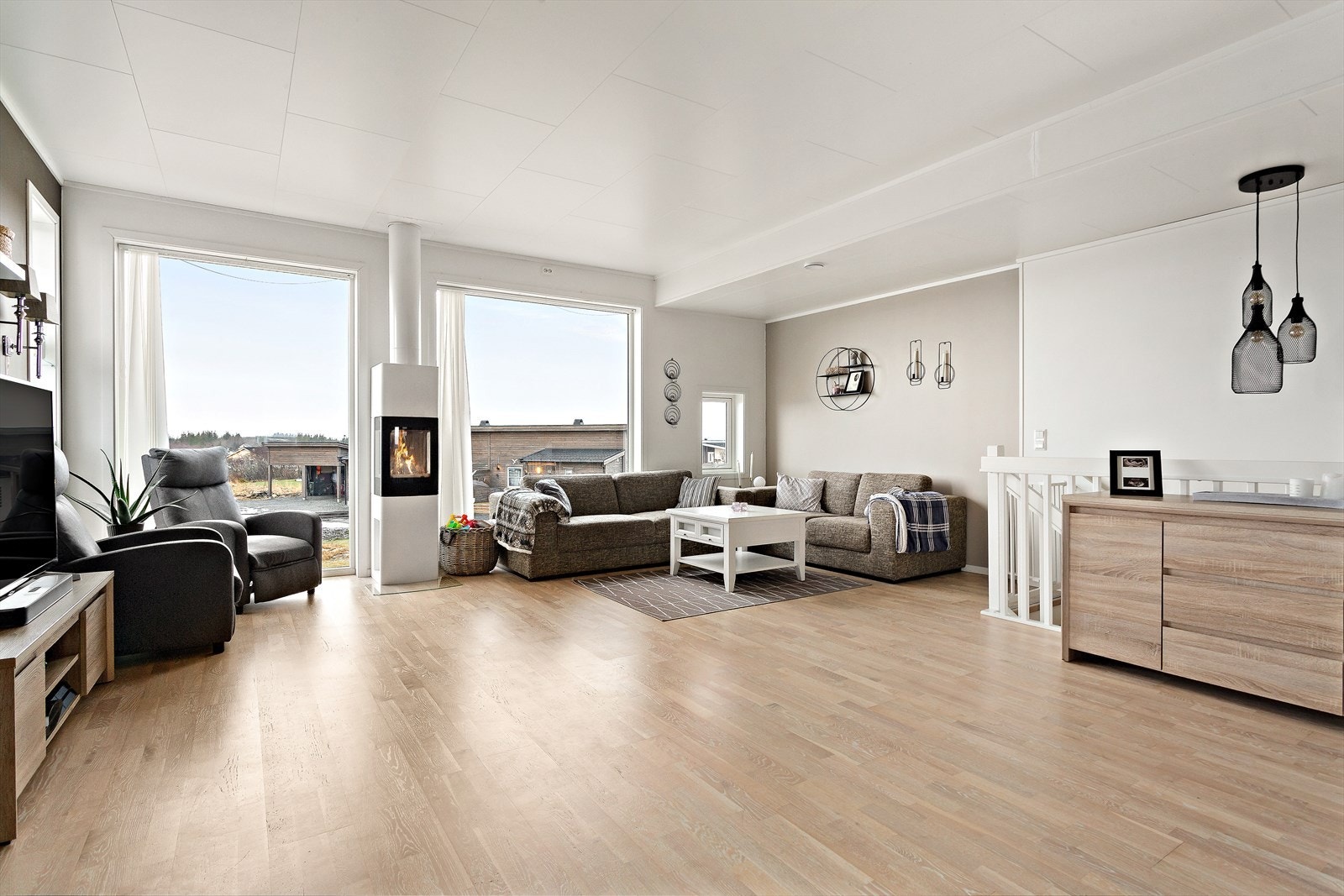 En pen og elegant vedovn er plassert mellom de store stuevinduene og kan sees fra hele stuen. En energieffektiv oppvarming av rommet Galleribilde