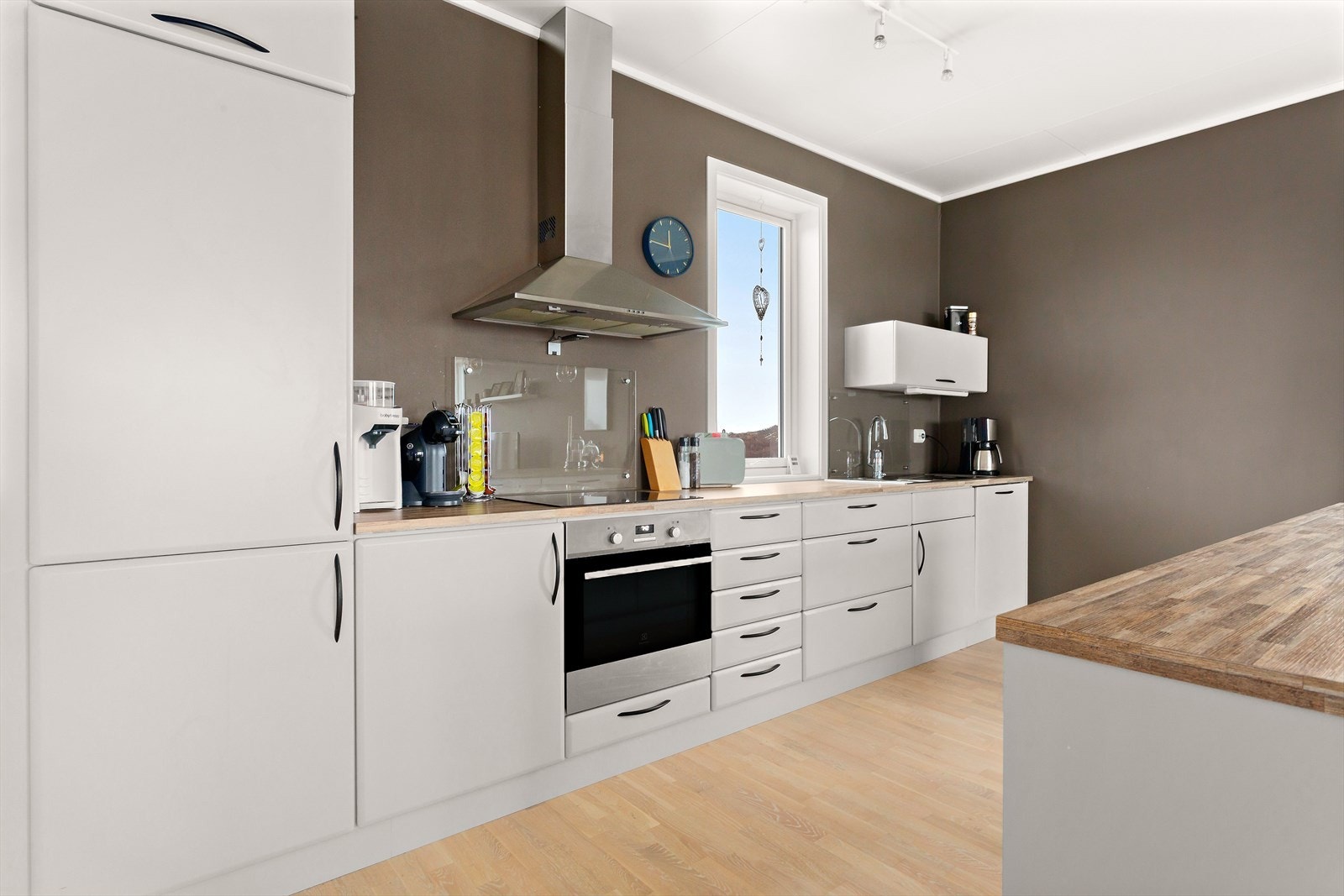 Fargevalget på kjøkkeninnredning har falt på en varm og lys gråfarge, arbeidssonene er praktisk plassert i forhold til hverandre Galleribilde