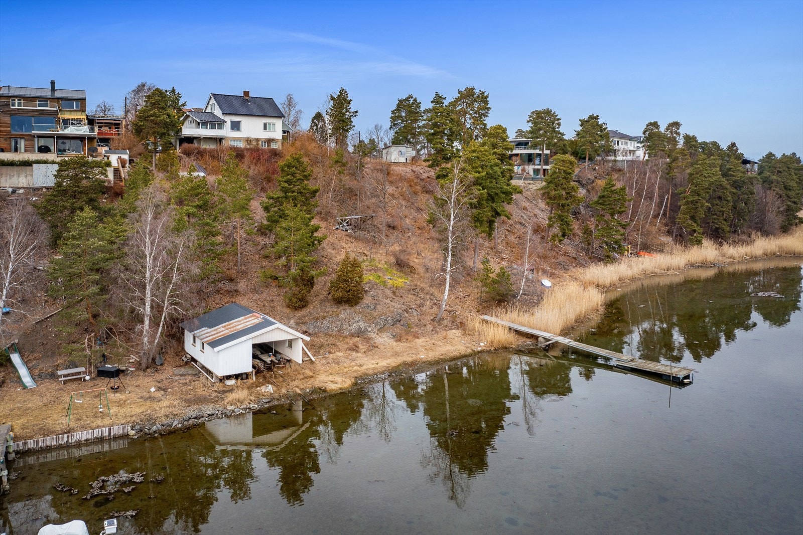 Tomt ned mot vannet med brygge /flytebrygge i vannkanten og frittstående naust/båthus. Galleribilde