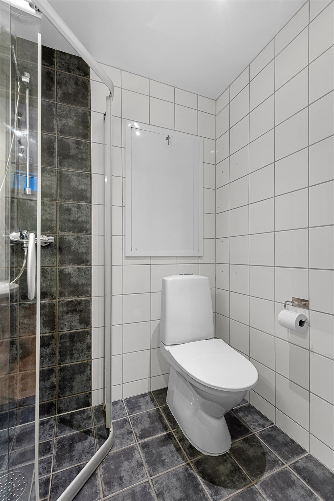 Med hvite og mørke fliser gir badet et tidløst uttrykk. Det er i tillegg varmekabler i gulv og nytt toalett fra 2023. Galleribilde