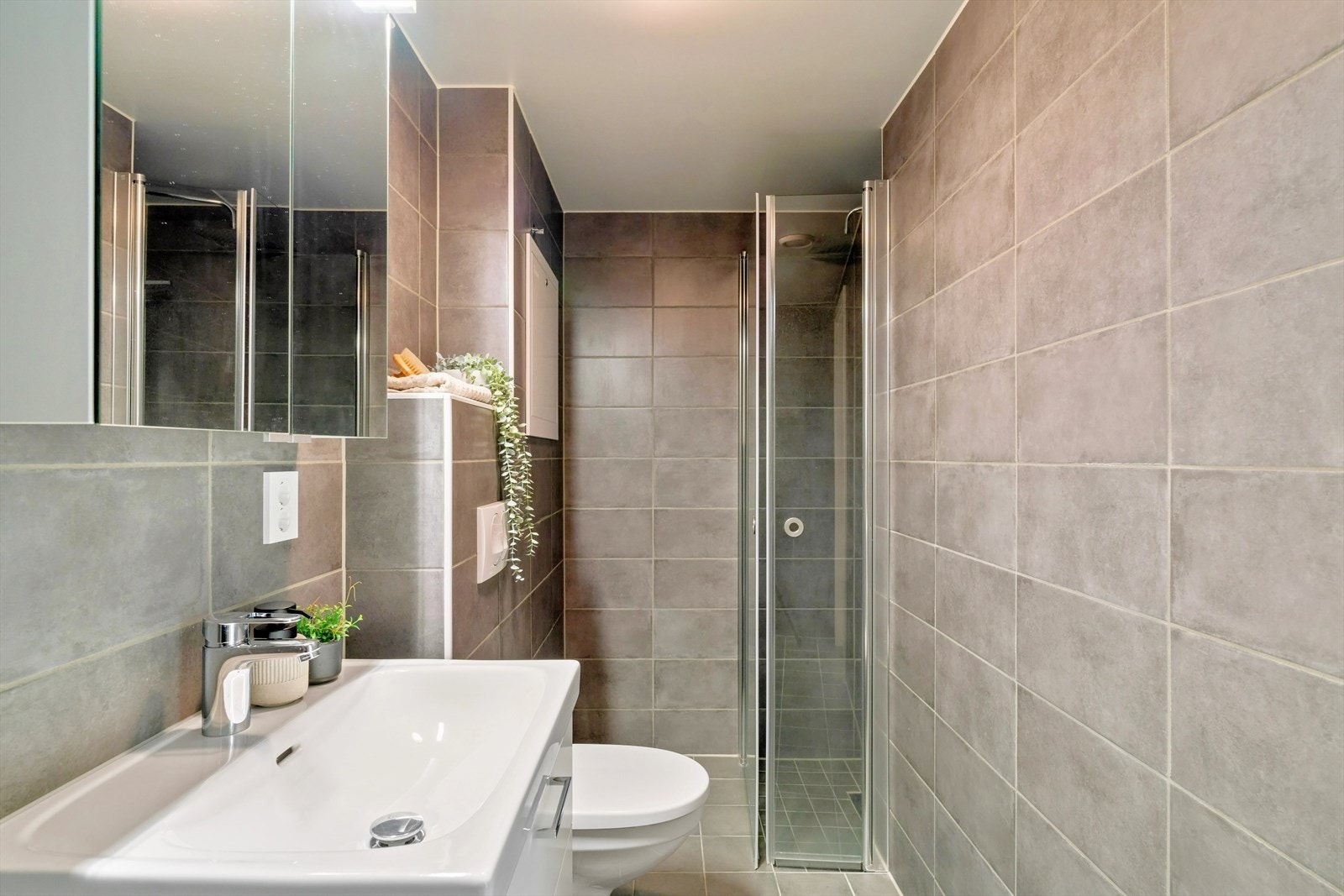 På badet har man vegghengt toalett, dusj, opplegg for vaskemaskin og baderomsinnredning med servant og overhengende speil med lagringsplass og belysning. Galleribilde