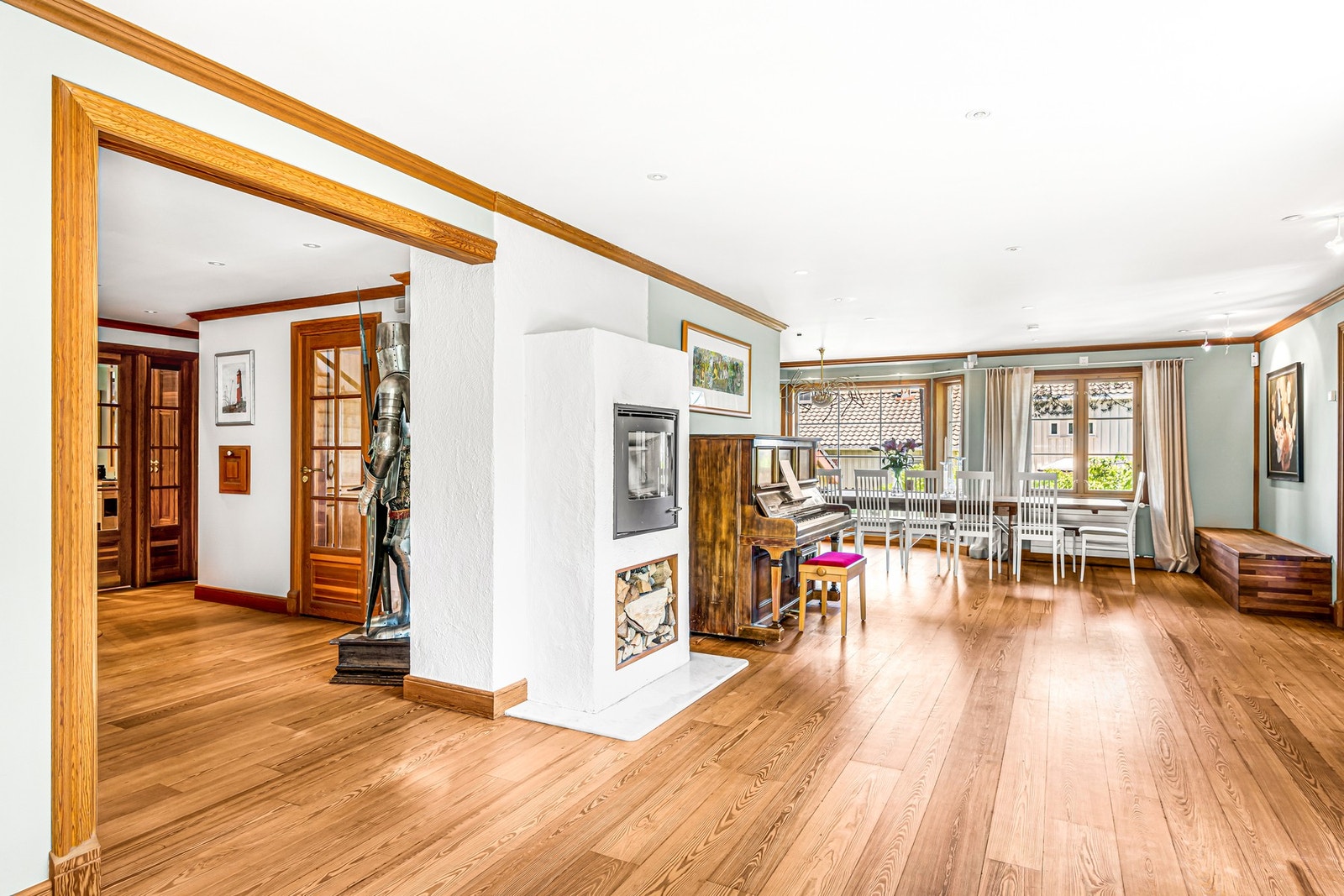 Stuen mot kjøkkendel. Rommet har vannbåren gulvvarme under spisebordet, radiatorer under og ved vinduer, og en rentbrennende peis med glassdør midt i rommet. Galleribilde