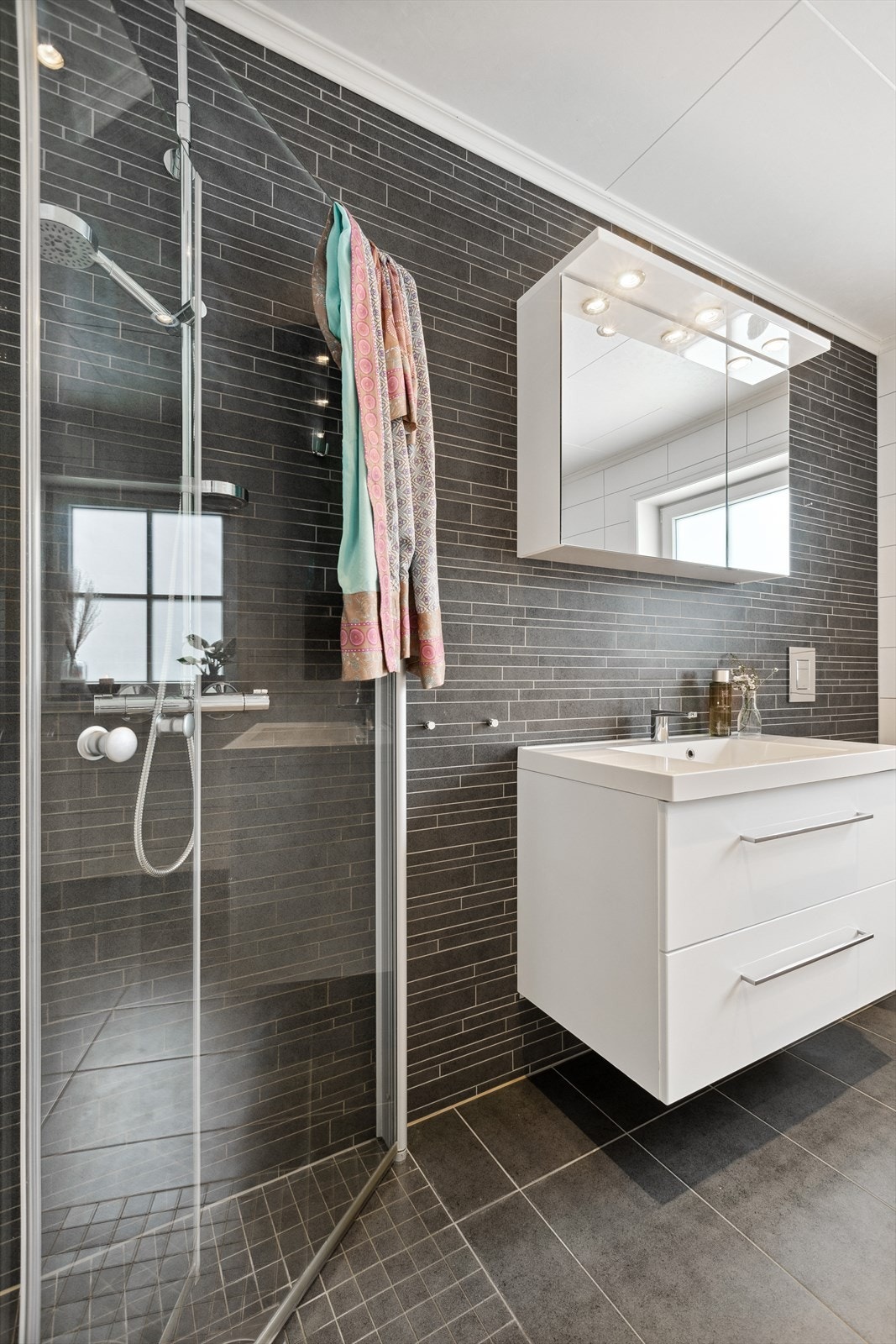 Badet i 1. etasje er innredet med veggmontert toalett, dusjhjørne med innsvingbare glassdører og servantinnredning med skuffer og speilskap. Galleribilde