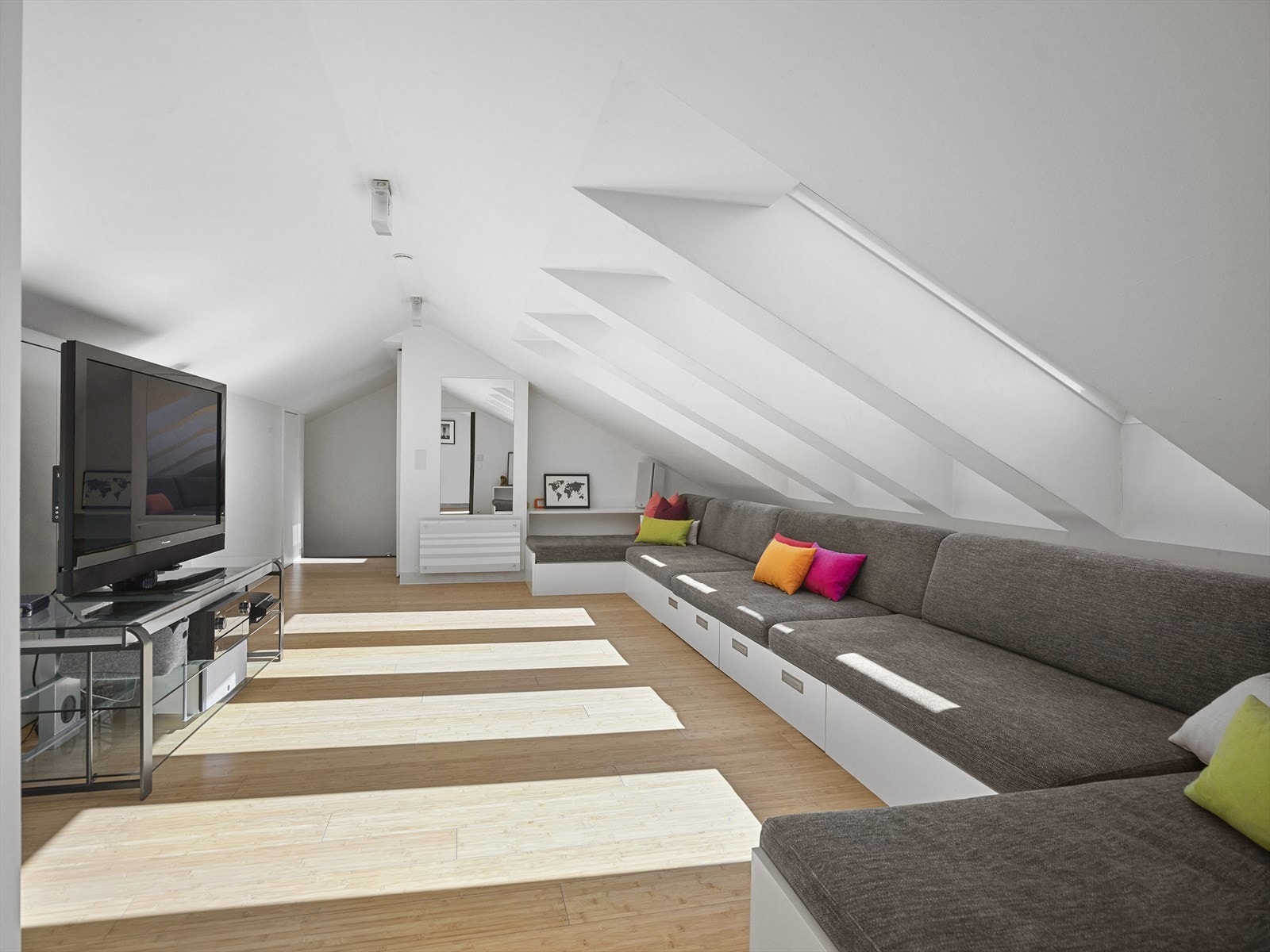 Lys og luftig stue på loft med plassbygget sofa med praktiske skuffer. Galleribilde