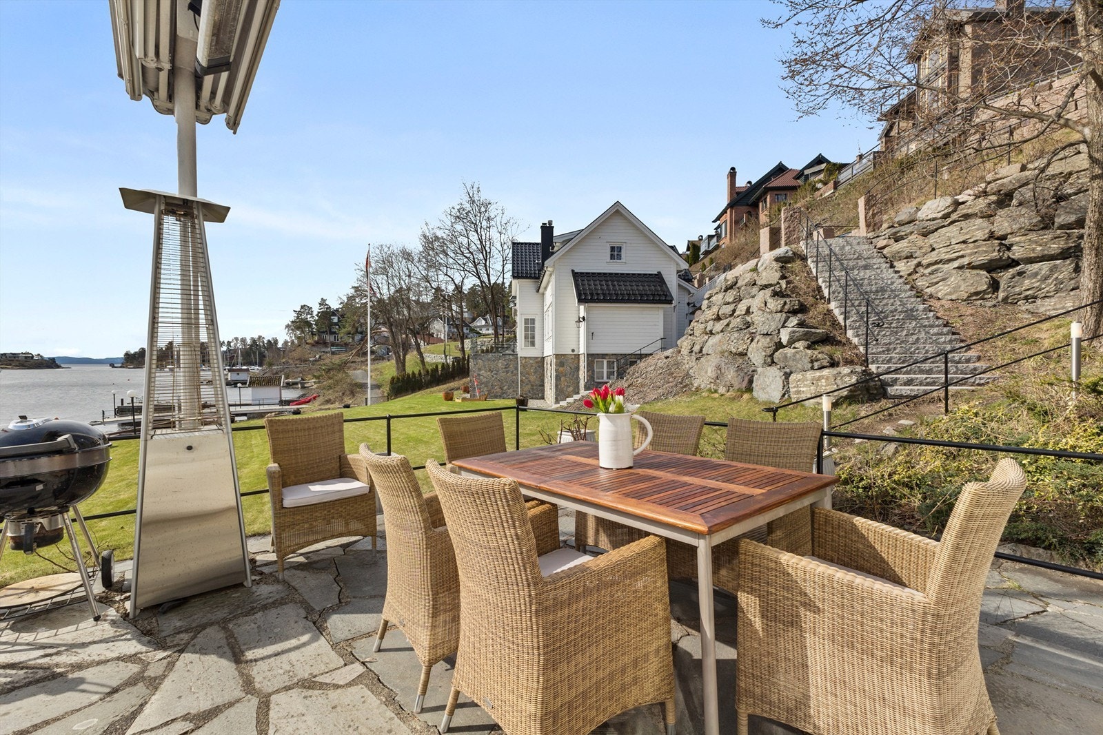 Boligen har en flott uteplass med utgang fra stuen. Her er det en skiferlagt terrasse med plass til både loungemøbler og spisebord. Videre adkomst til hagen og fjorden nedenfor. Galleribilde