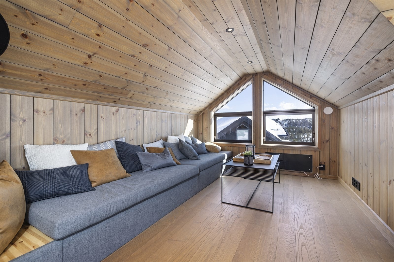 Loftstue med lang plassbygget sofa og store vindusflater. Galleribilde