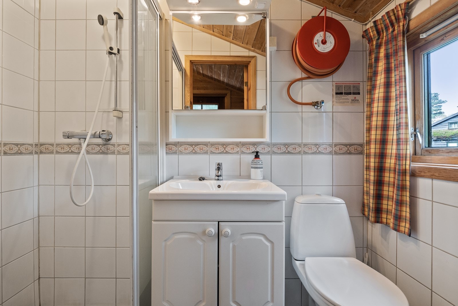 Flislagt baderom fra byggeår. Det er utstyrt med dusjhjørne, gulvmontert toalett og servantinnredning med heldekkende servant og speilskap over. Galleribilde