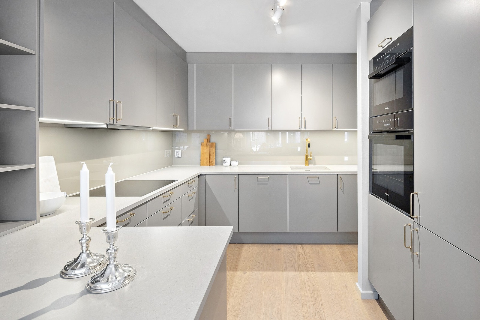 Elegant kjøkken fra HTH med parkett på gulv og glass på vegg over benk. Mekanisk avtrekk over stekesonen. Benkeplate i Silestone og armatur fra Tapwell i messing. Galleribilde