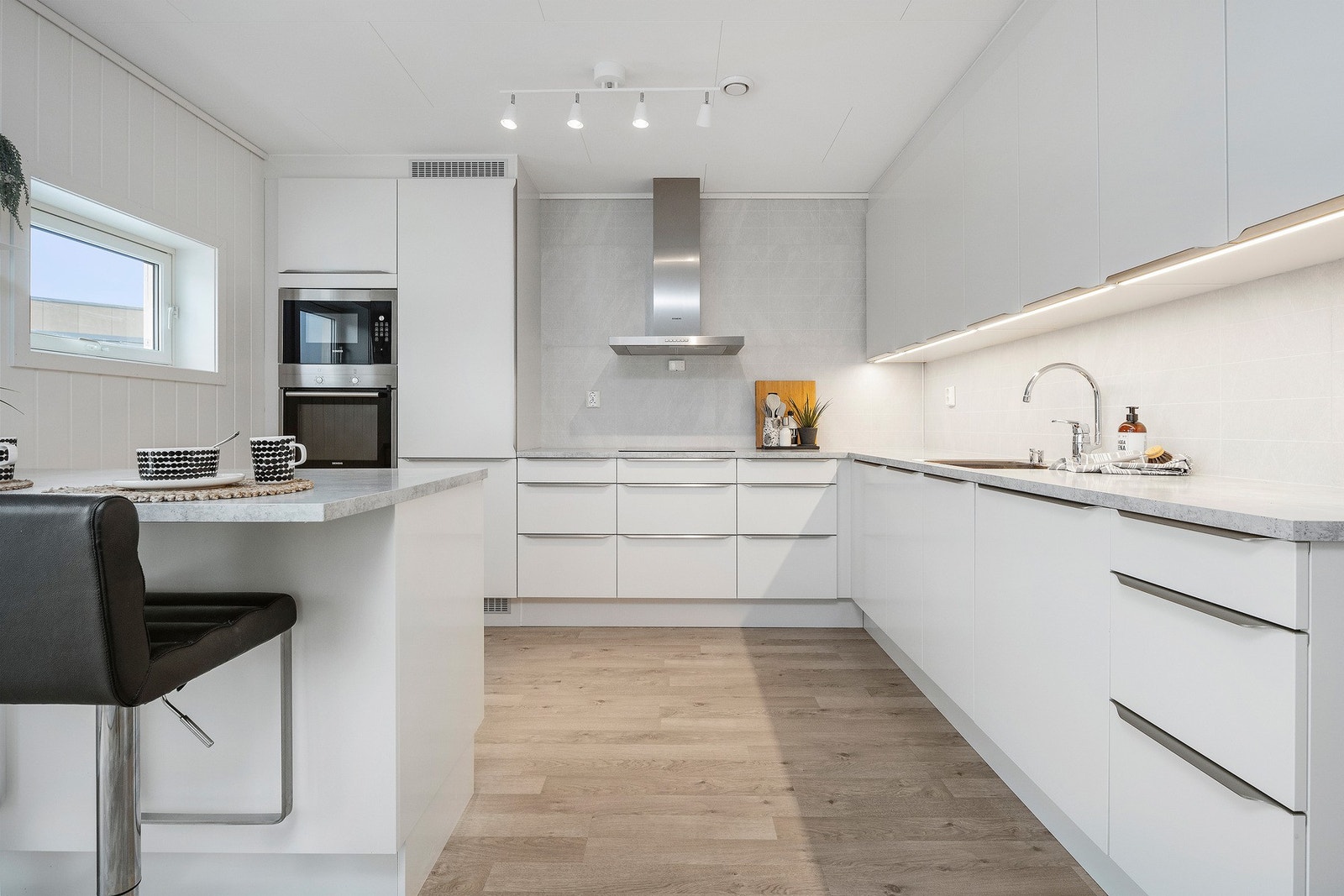 Moderne og stilrent kjøkken med integrerte hvitevarer, høyskap og flis som backsplash. Galleribilde