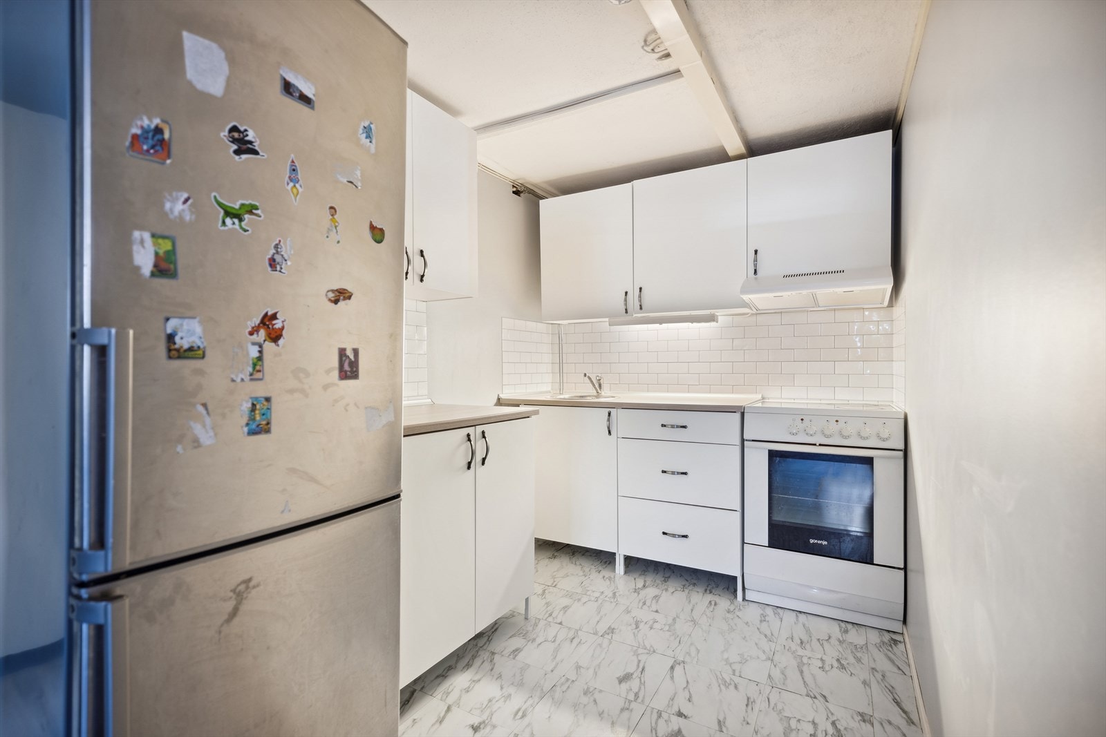 Fin kjøkkenavdeling med ny innredning i 2023, med hvite slette fronter og laminerte benkeplater. I innredningen er det opplegg og plass til komfyr og frittstående kjøleskap. Galleribilde