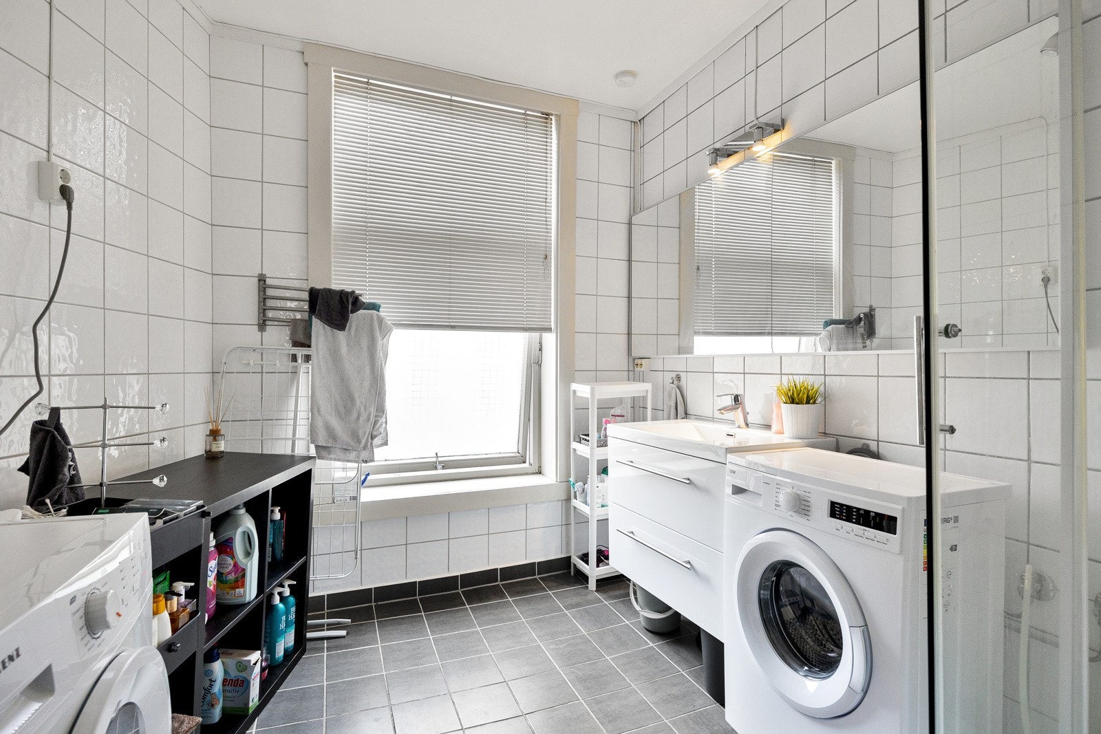Romslig, flislagt bad med varmekabler på bad. Badet består av toalett, servant med benkeskap, dusjkabinett og opplegg til vaskemaskin. Galleribilde