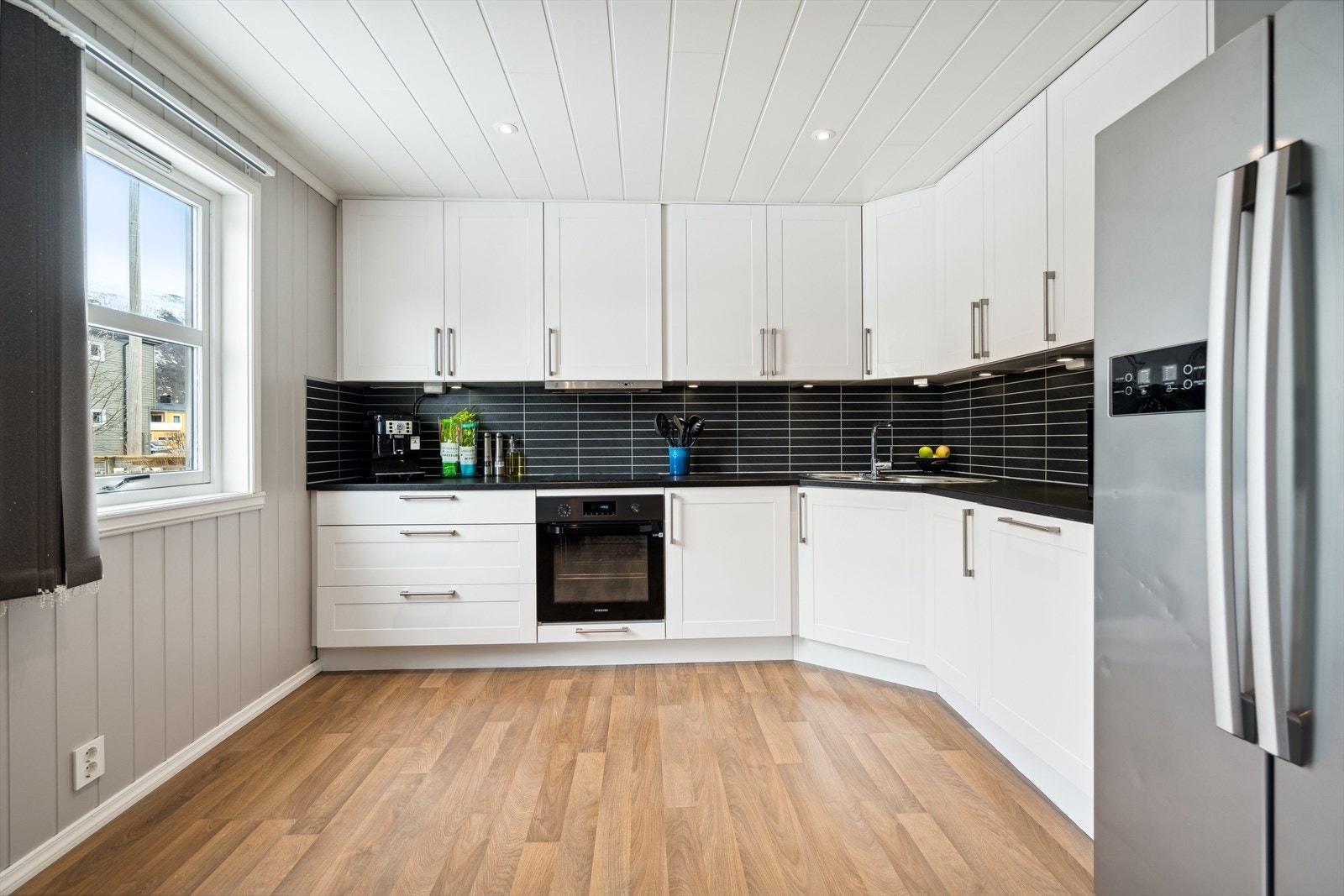 Kjøkkenet har en stilren takhøy innredning med profilerte hvite fronter og laminert benkeplate. Integrert komfyr og oppvaskmaskin. Galleribilde