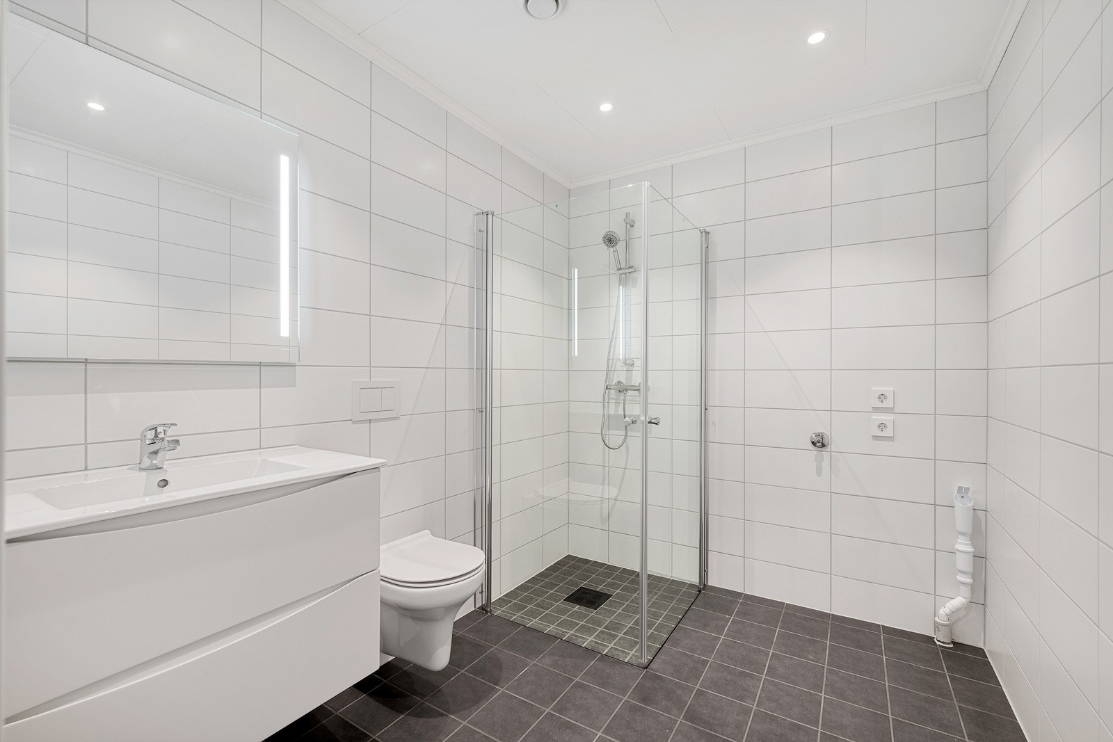 Flott flislagt bad med servant, vegghengt toalett, dusjhjørne og opplegg til vaskemaskin. Galleribilde