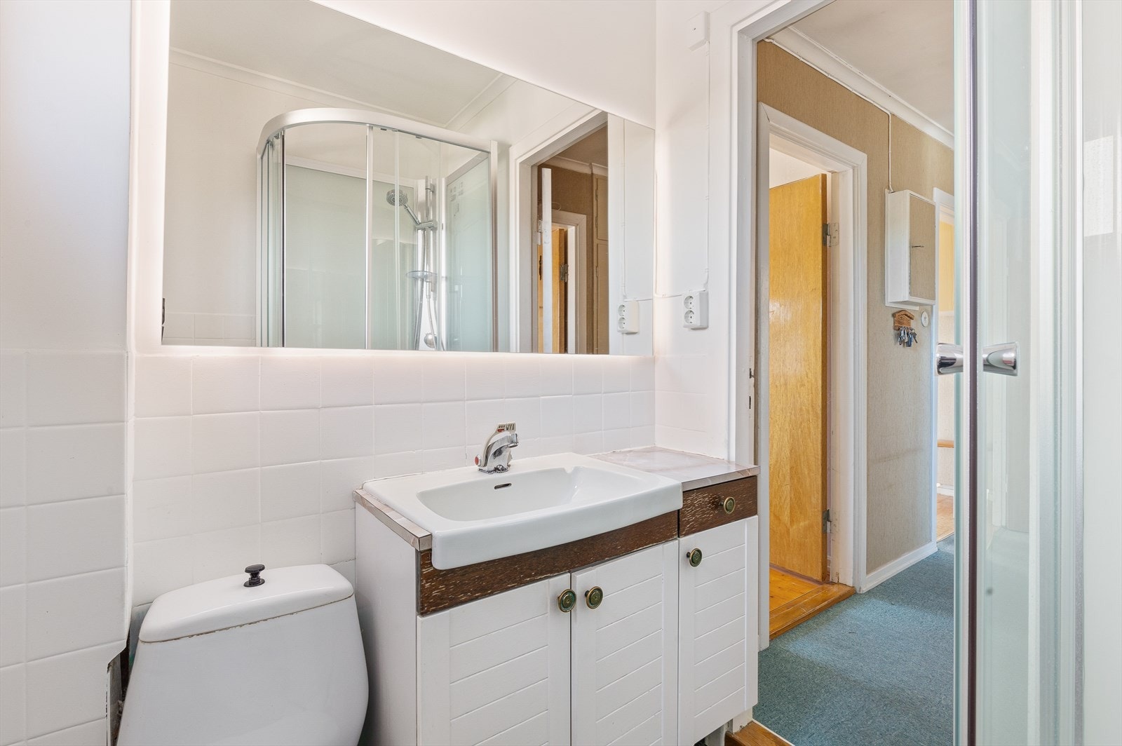 Badet har speil med indirekte belysning, servant på skapmøblement, gulvmontert toalett og et dusjkabinett. Galleribilde