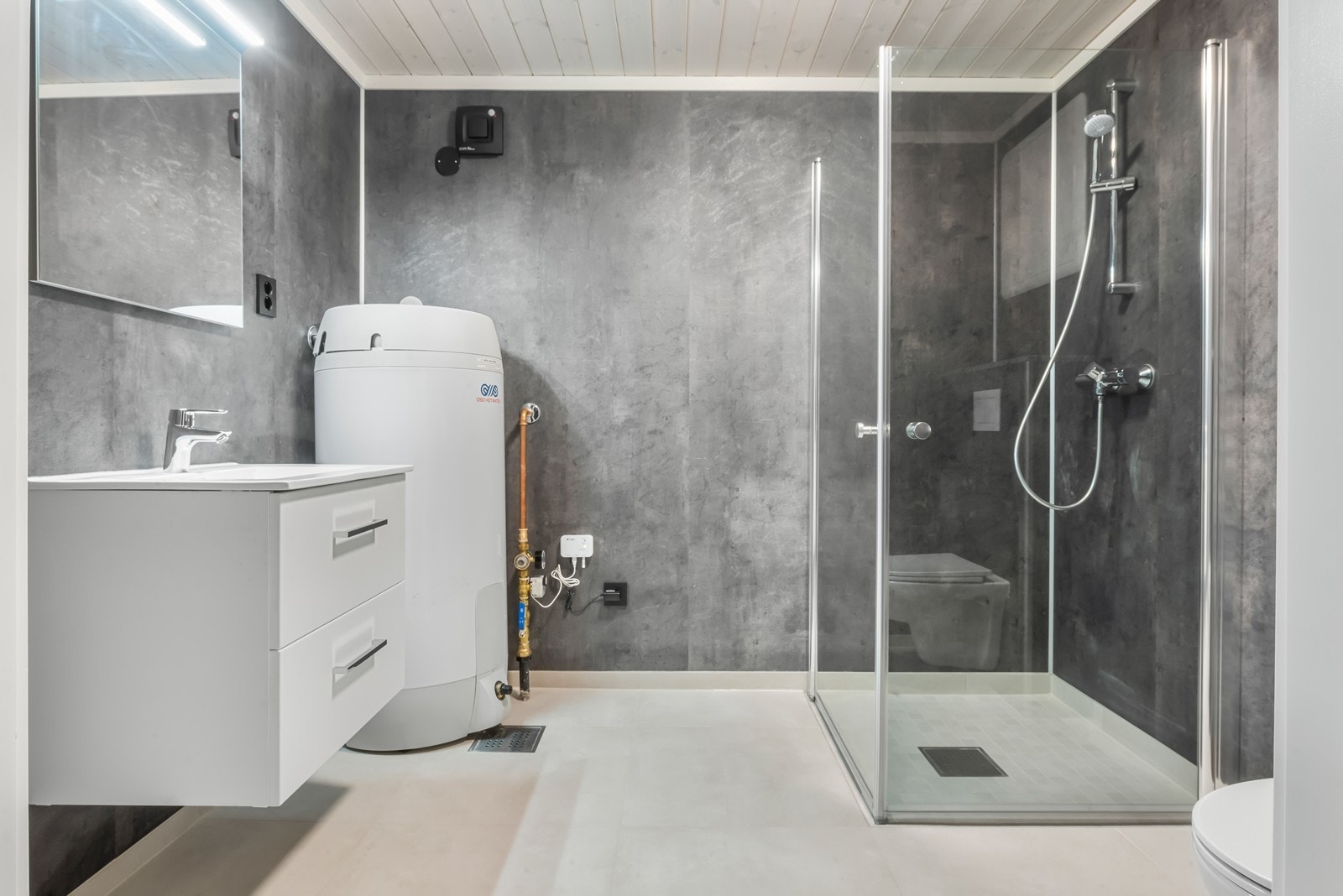 Flislagt bad med varmekabler i gulv, opplegg til vaskemaskin, servant med skuffer, varmtvannsbereder. Galleribilde