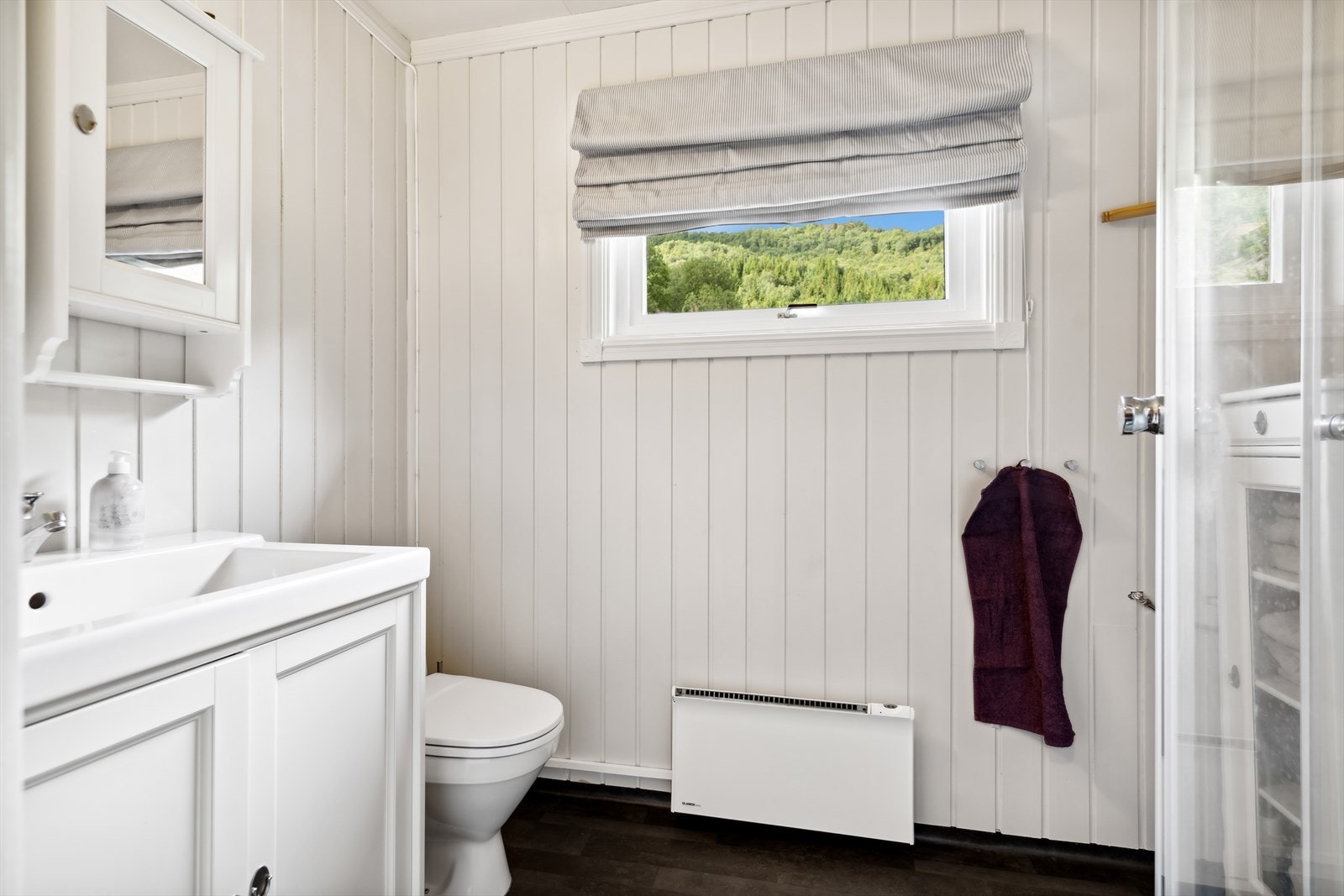 Badet er stilrent med vinylbelegg på gulv og hvitmalt panel/tømmer på vegger Galleribilde