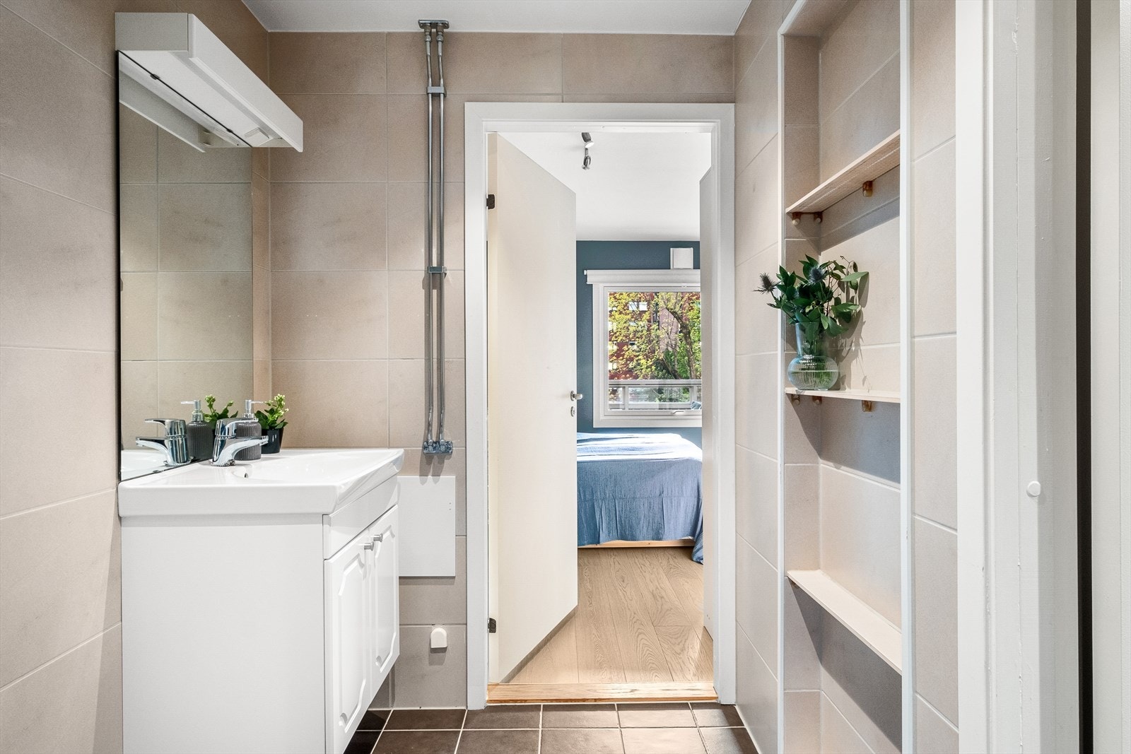 Badet har innredning og garnityr som består av gulvstående toalett, dusjhjørne med innfellbare glassdører og servantinnredning med skap, servant og speil med lys og stikkontakt Galleribilde