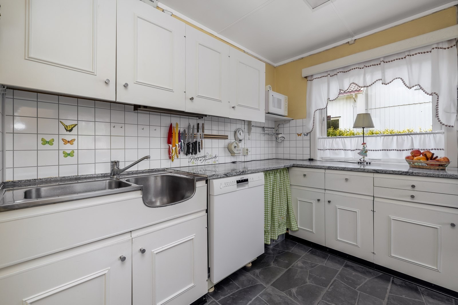 Kjøkkenet har innredning med hvite profilerte fronter, laminert benkeplate og heltrukket benkebeslag, samt flis over kjøkkenbenk. Det er kjøkkenventilator med avtrekk ut. Galleribilde
