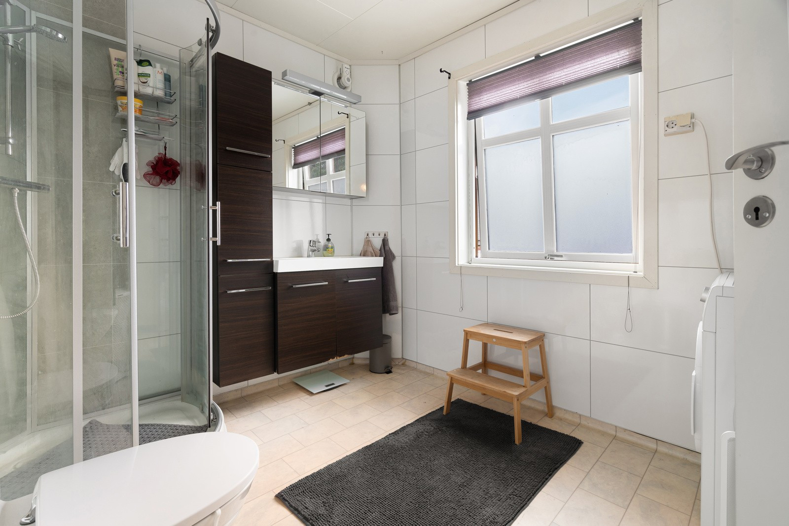 Badet i 1. etasje har gulvvarme og innredet med mørk baderomsinnredning, dusjkabinett og gulvmontert toalett.