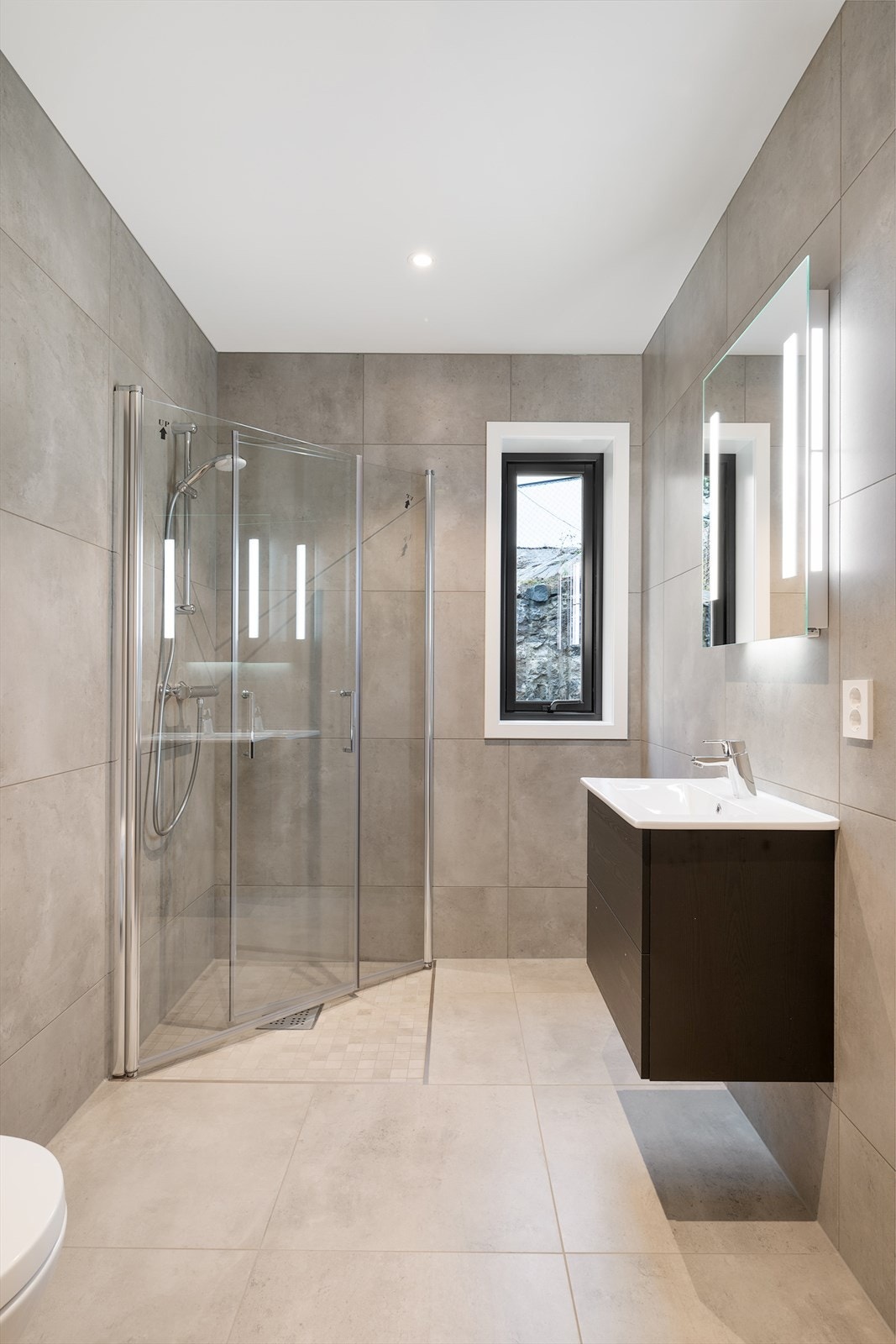 Badet i 1.etg har vegger og gulv kledd med store fliser i en lun sandfarge, som erstattes med mindre fliser i dusjhjørne. Galleribilde
