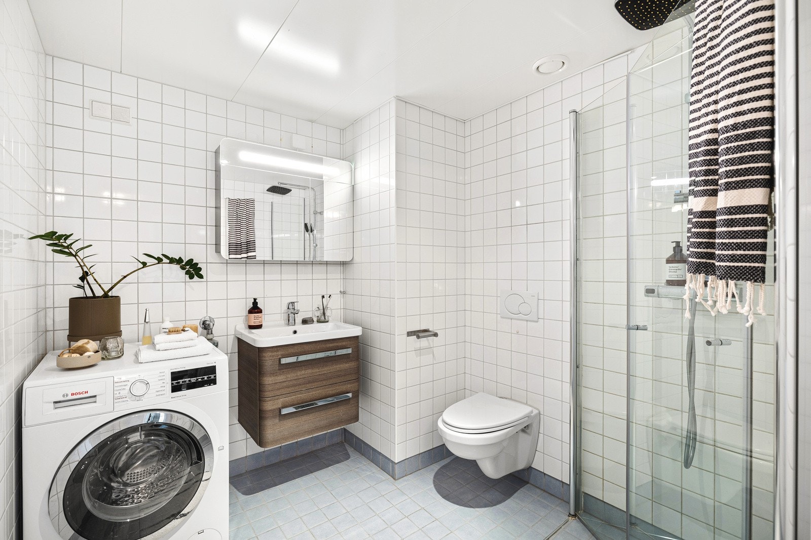 Flislagt baderom med dusjhjørne, vegghengt klosett, servant og opplegg for vaskemaskin. "Alt" et baderom bør ha. Galleribilde