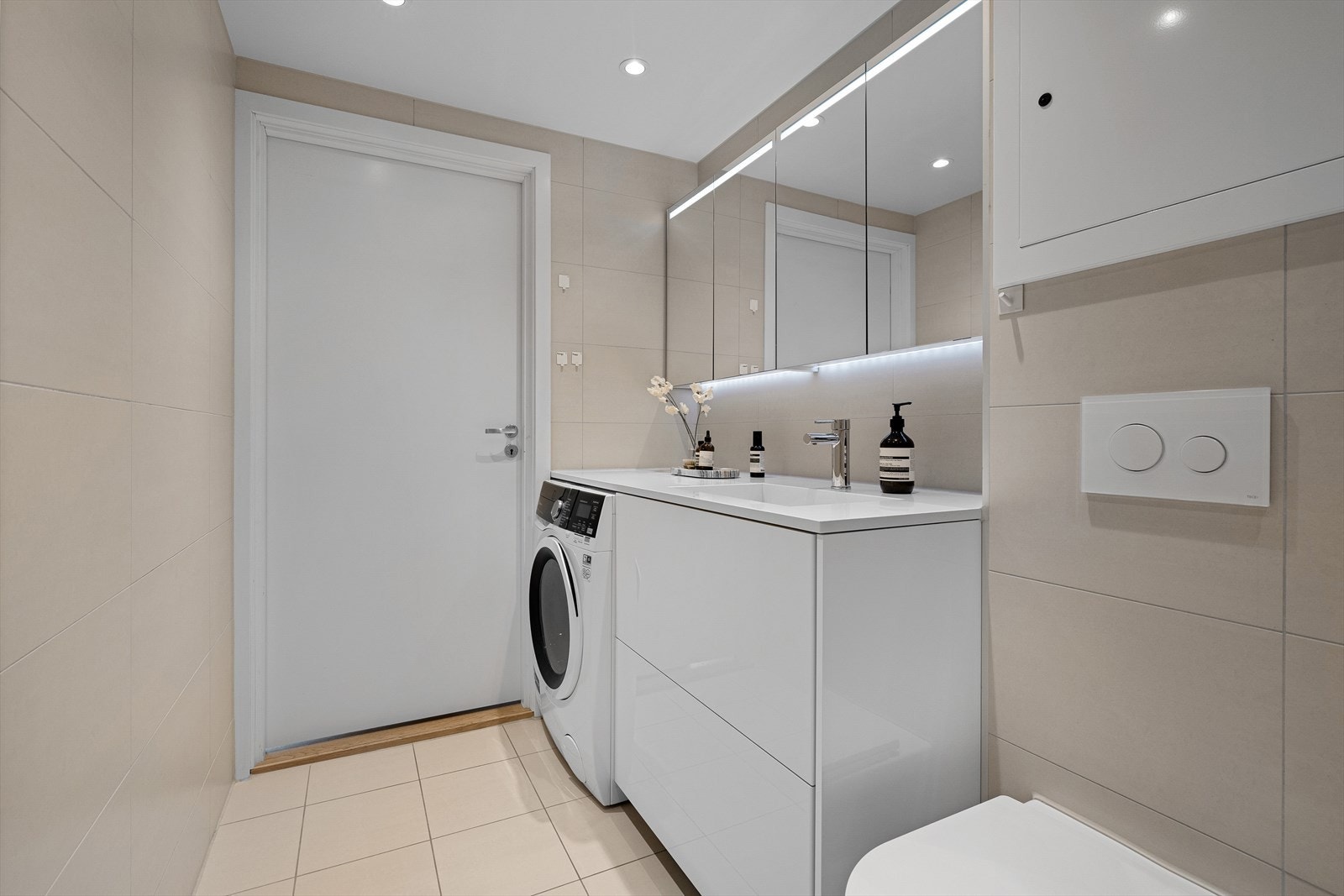 Legg merke til benkeplaten som gir deg ekstra oppbevaringsplass over vaskemaskinen. To doble speilskap over, med integrert belysning. Galleribilde