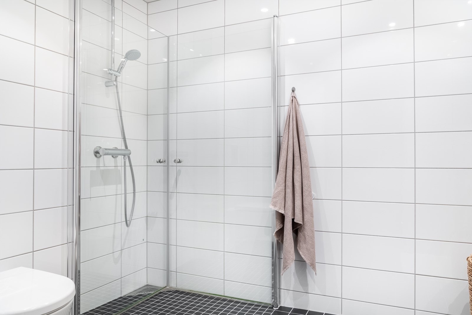 Badet inneholder toalett, helstøpt servant, skuffer under servant, dusjdører i klart glass og opplegg for vaskemaskin. Galleribilde