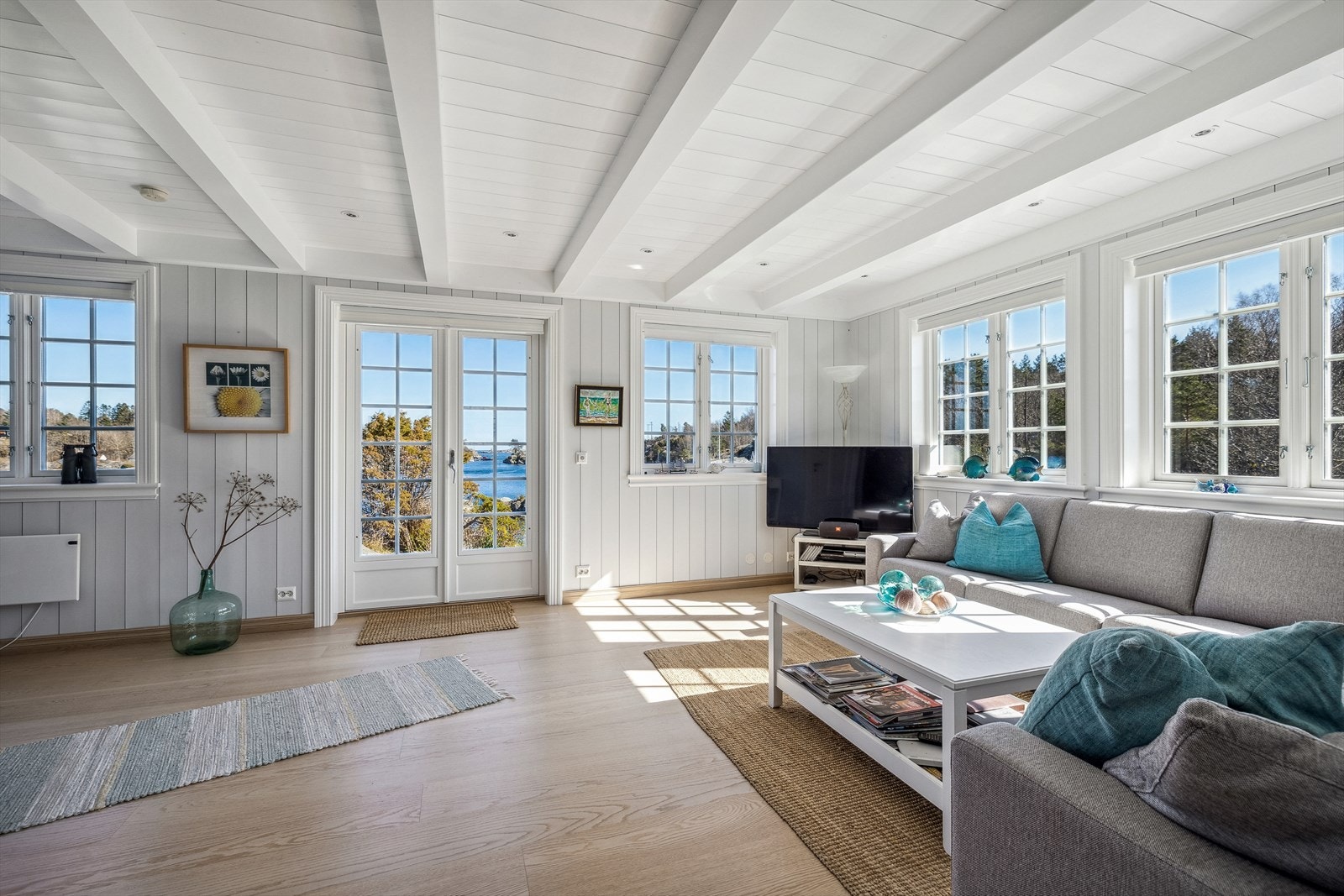 En lys og innbydende stue med malt panel på vegger og i himling Galleribilde