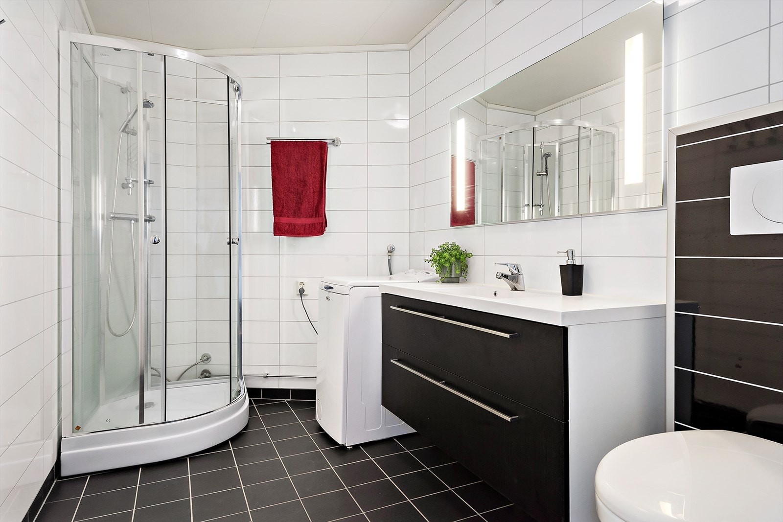 Badet har en moderne og tidløs utførelse med sorte flis på gulv og hvite våtromsplater. Romslig baderomsinnredning og opplegg for vaskemaskin. Galleribilde