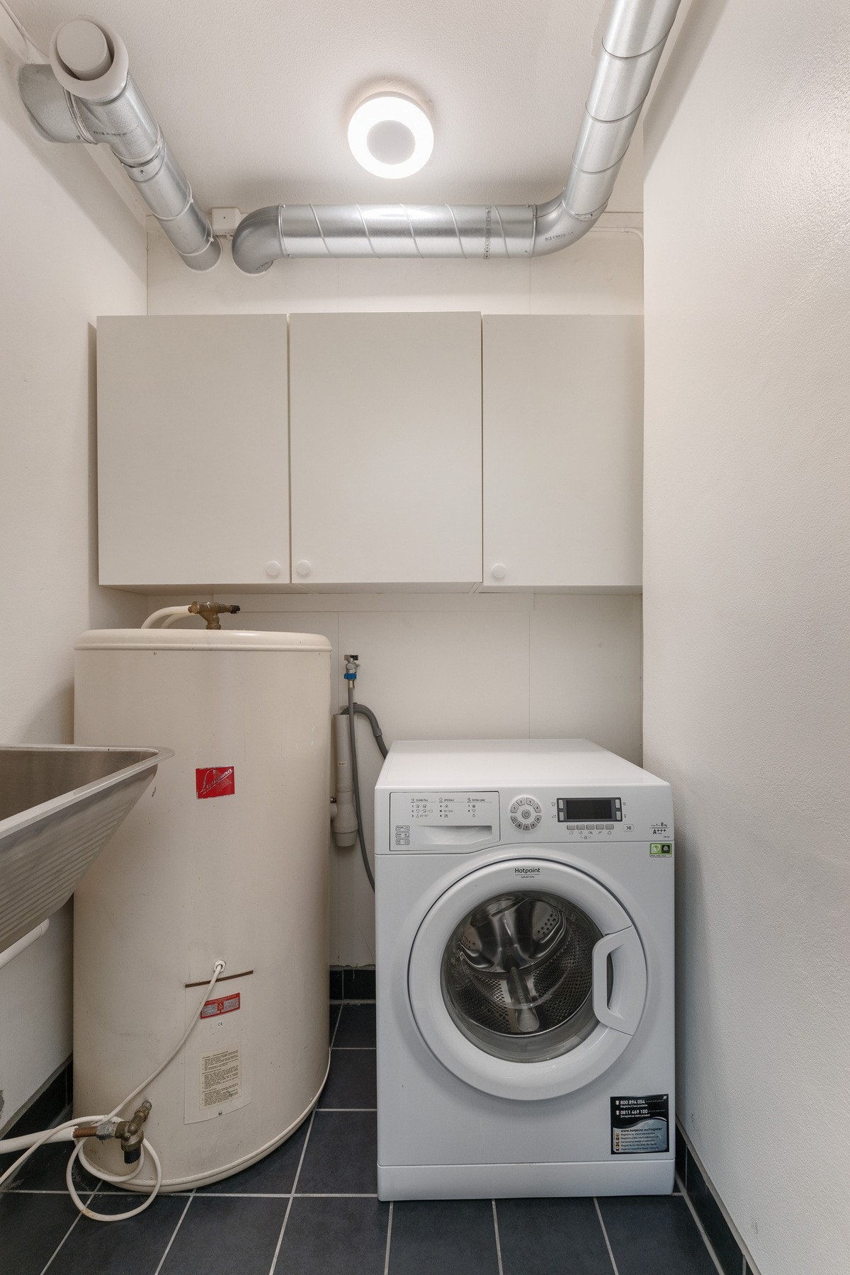 Vegg i vegg med badet er det et praktisk vaskerom på 2 kvm. Flis på gulv, varmtvannsbereder, skyllekum og opplegg til vaskemaskin. Galleribilde